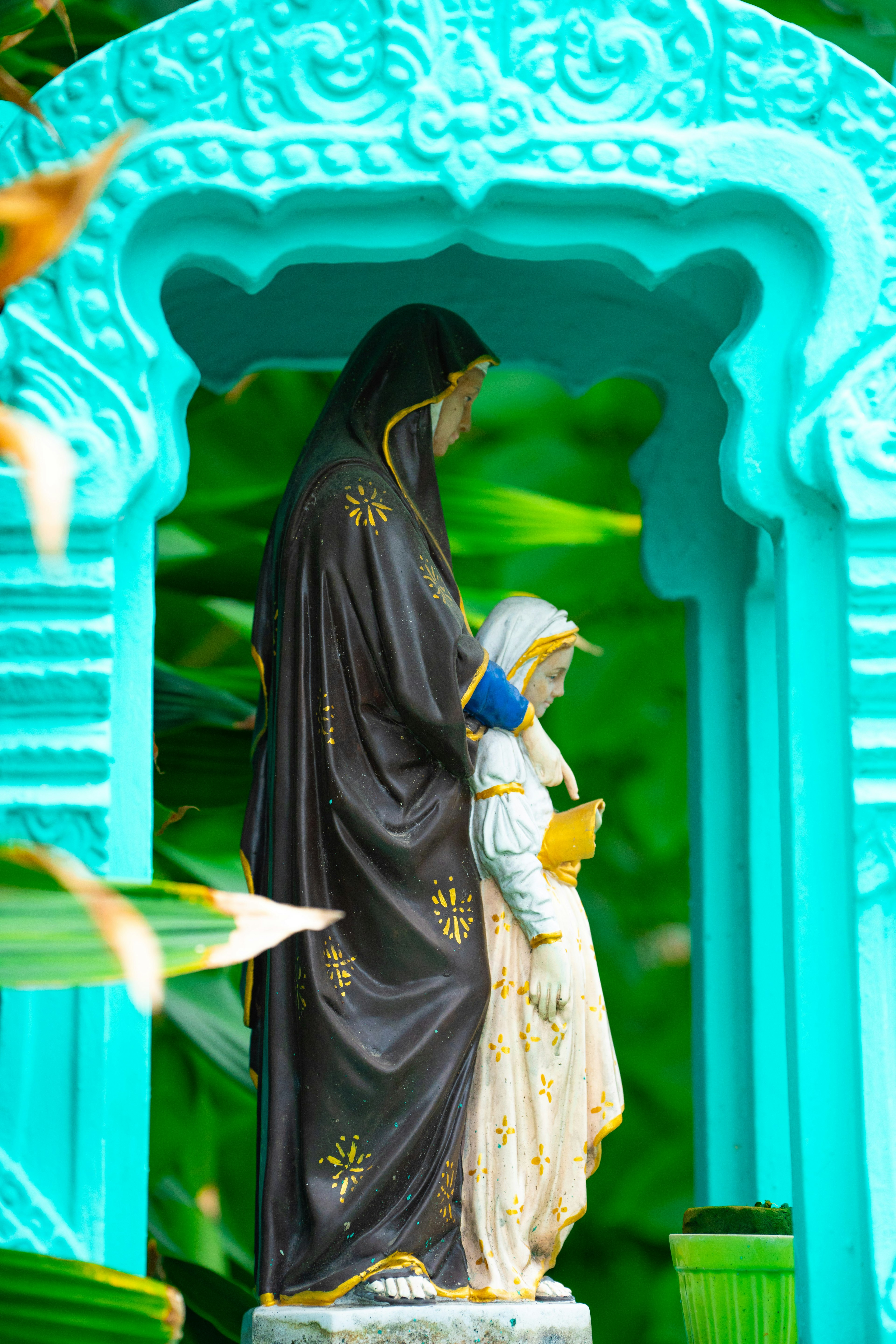 Statue of Virgin Mary and child in turquoise arch surrounded by green foliage