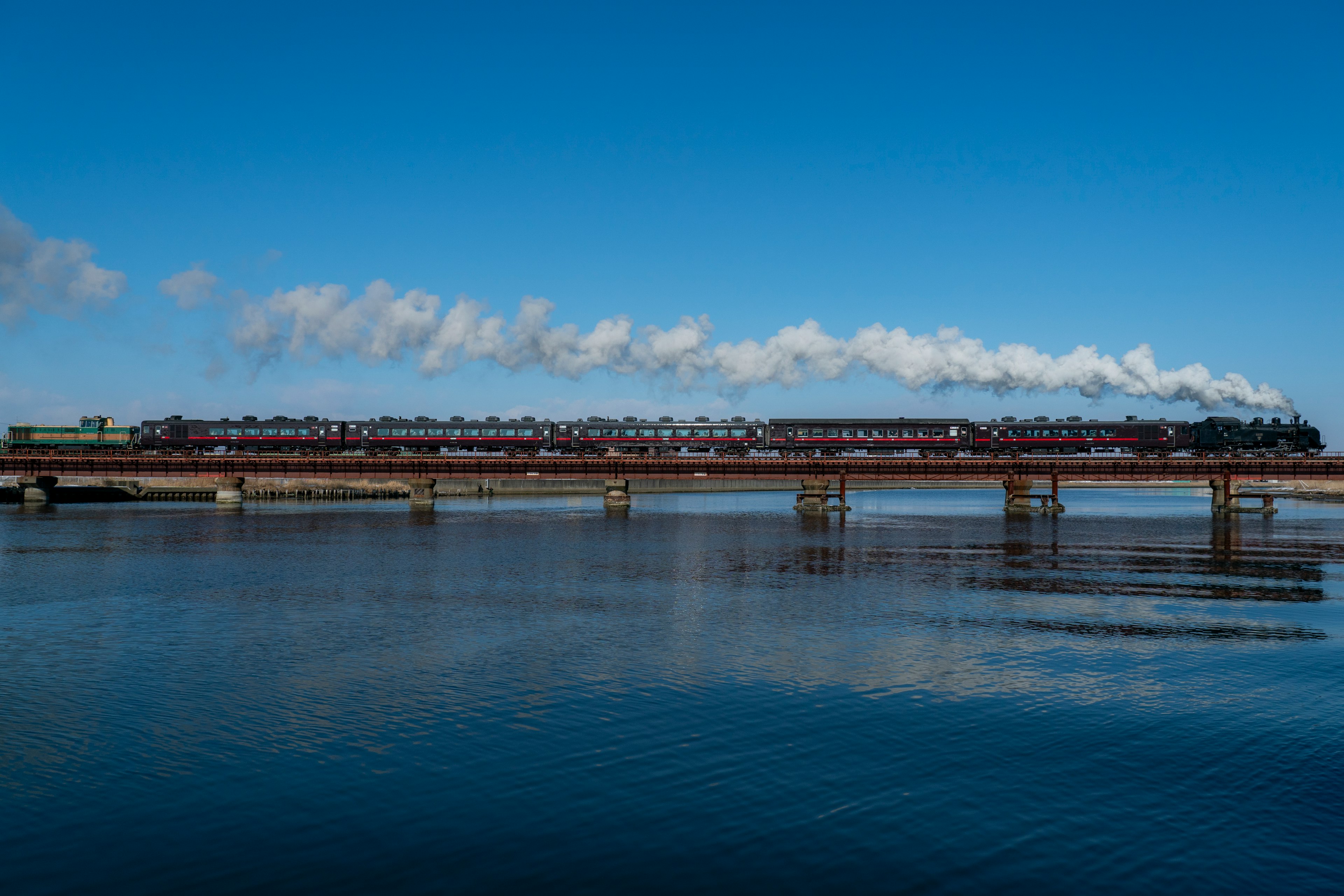 Locomotora de vapor cruzando un puente sobre un río con cielo azul claro