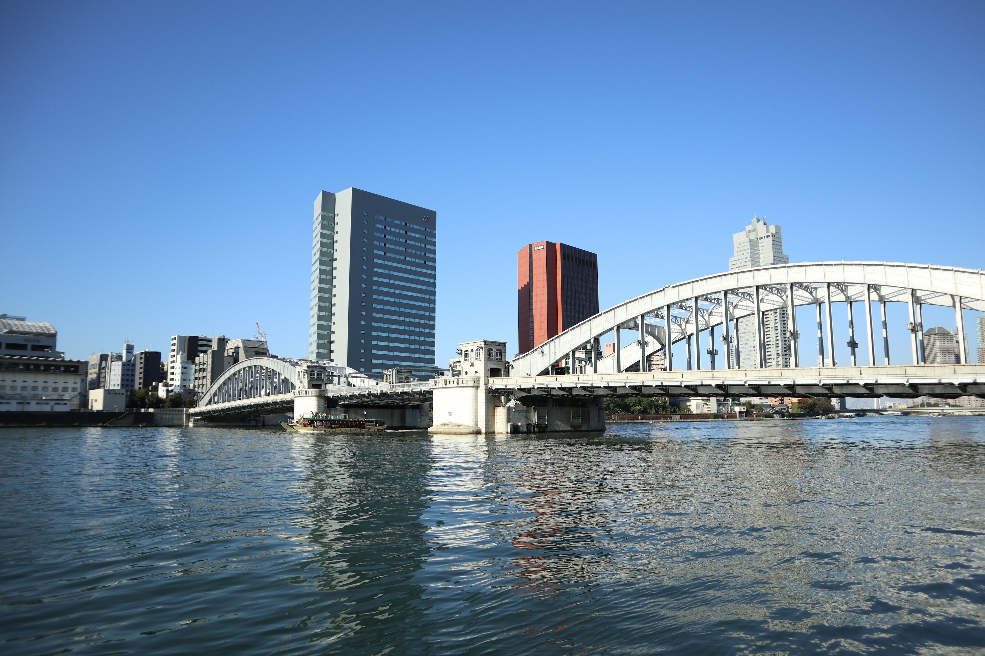 Bridge and skyscrapers reflecting on water under blue sky