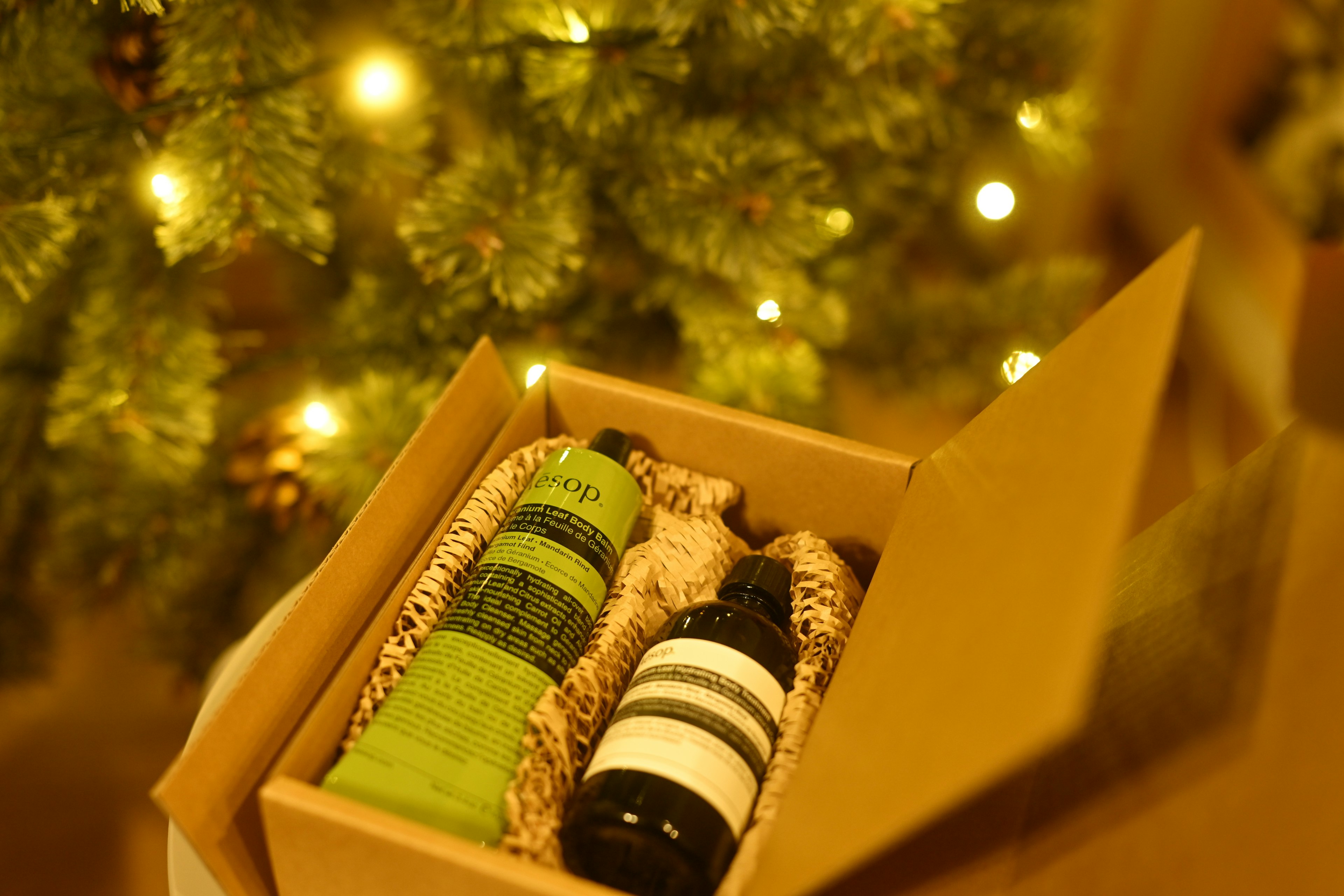 Caja abierta con toallas verdes y una botella frente a un árbol de Navidad