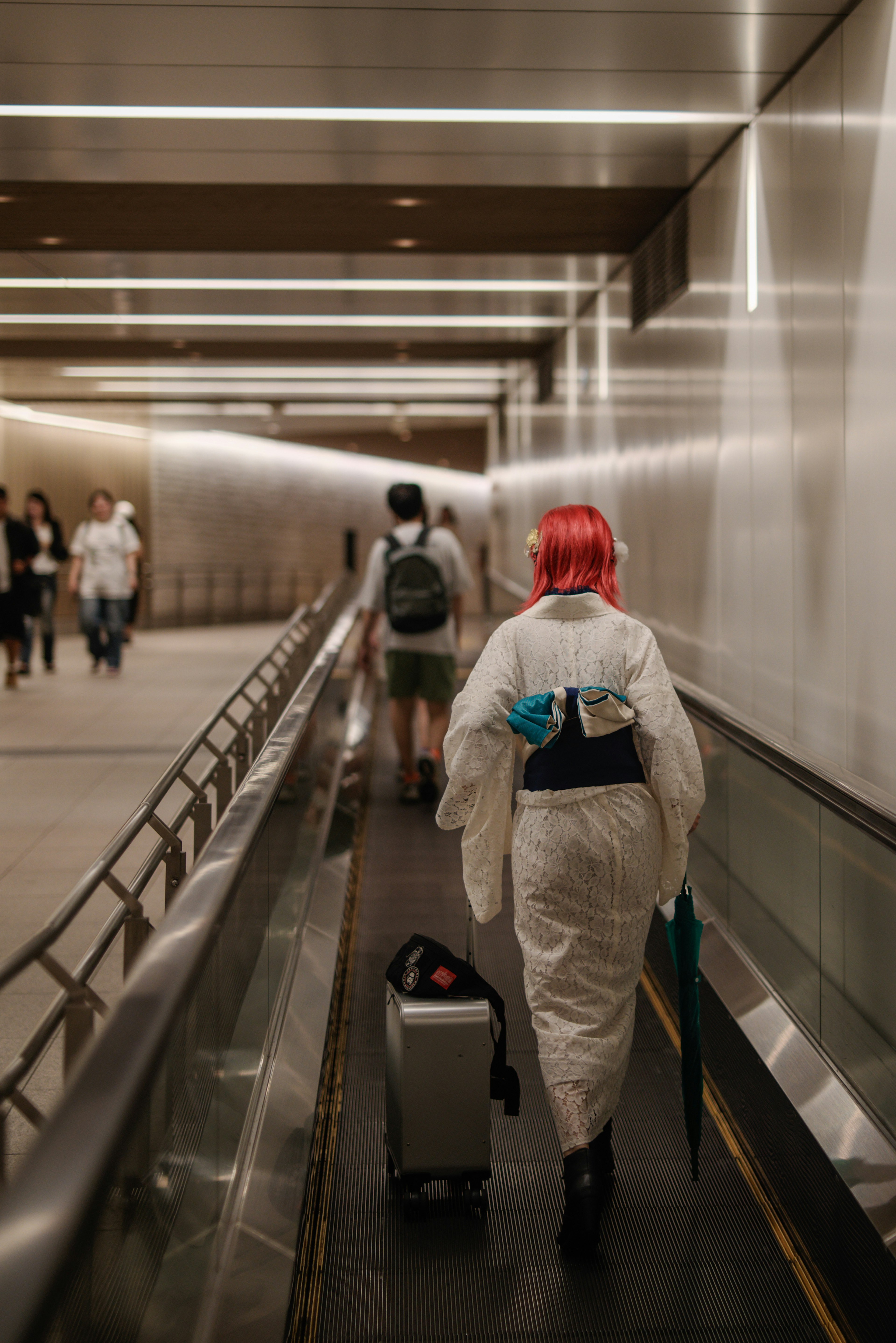 Un personnage aux cheveux rouges tirant une valise dans un couloir moderne