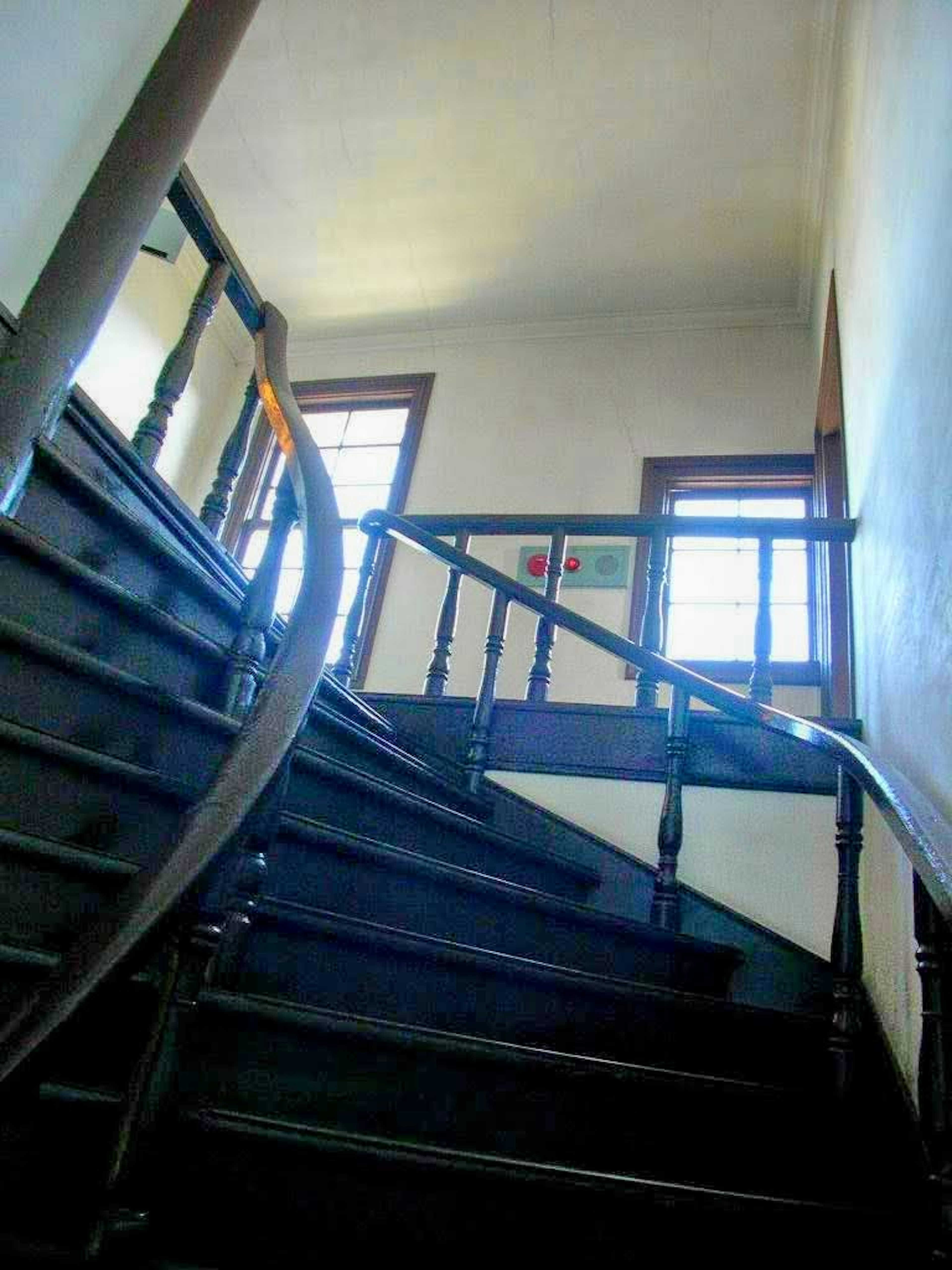 Image of a staircase viewed from an upward angle featuring wooden railings and steps natural light coming through windows