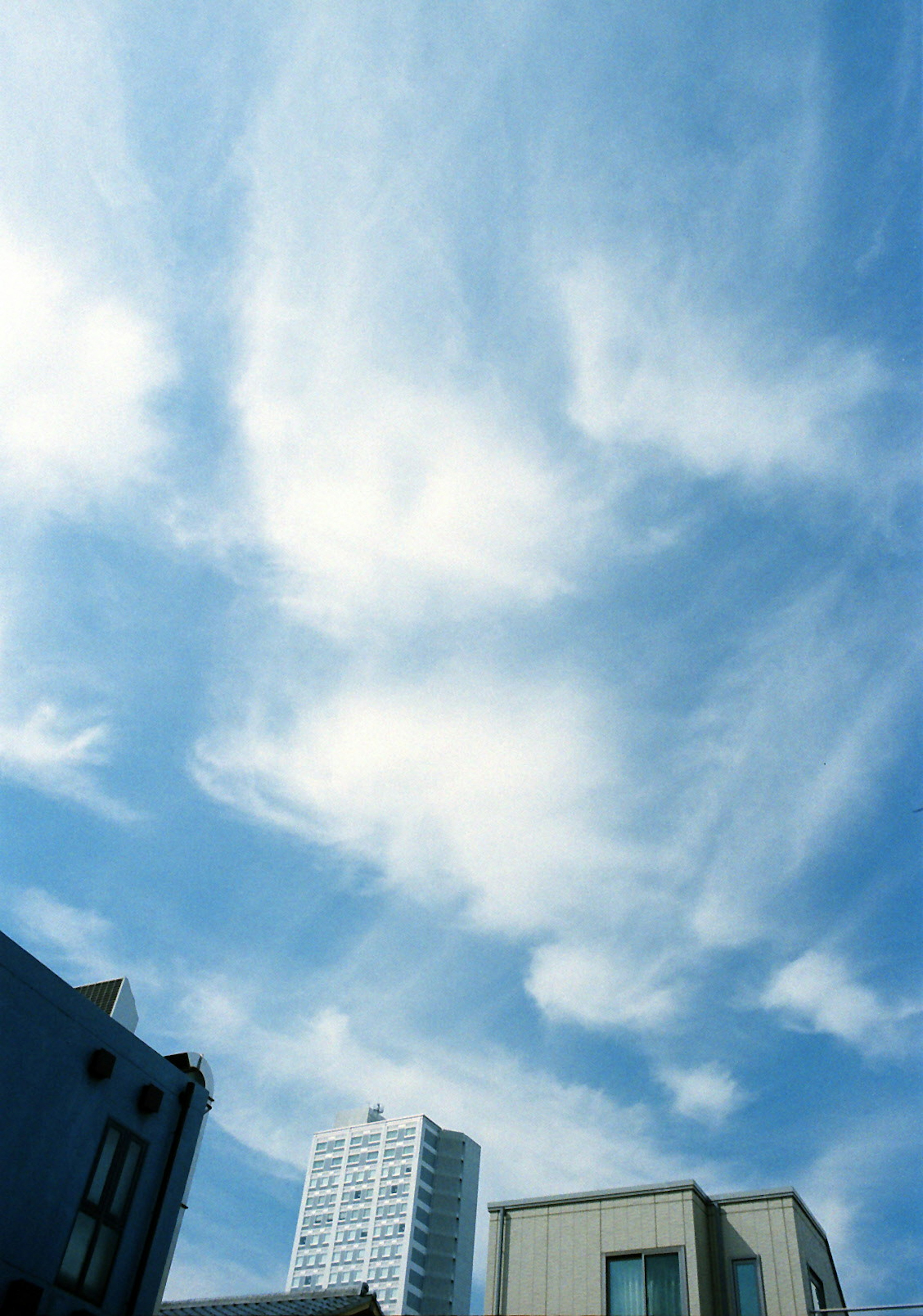 Awan putih mengalir di langit biru dengan siluet bangunan