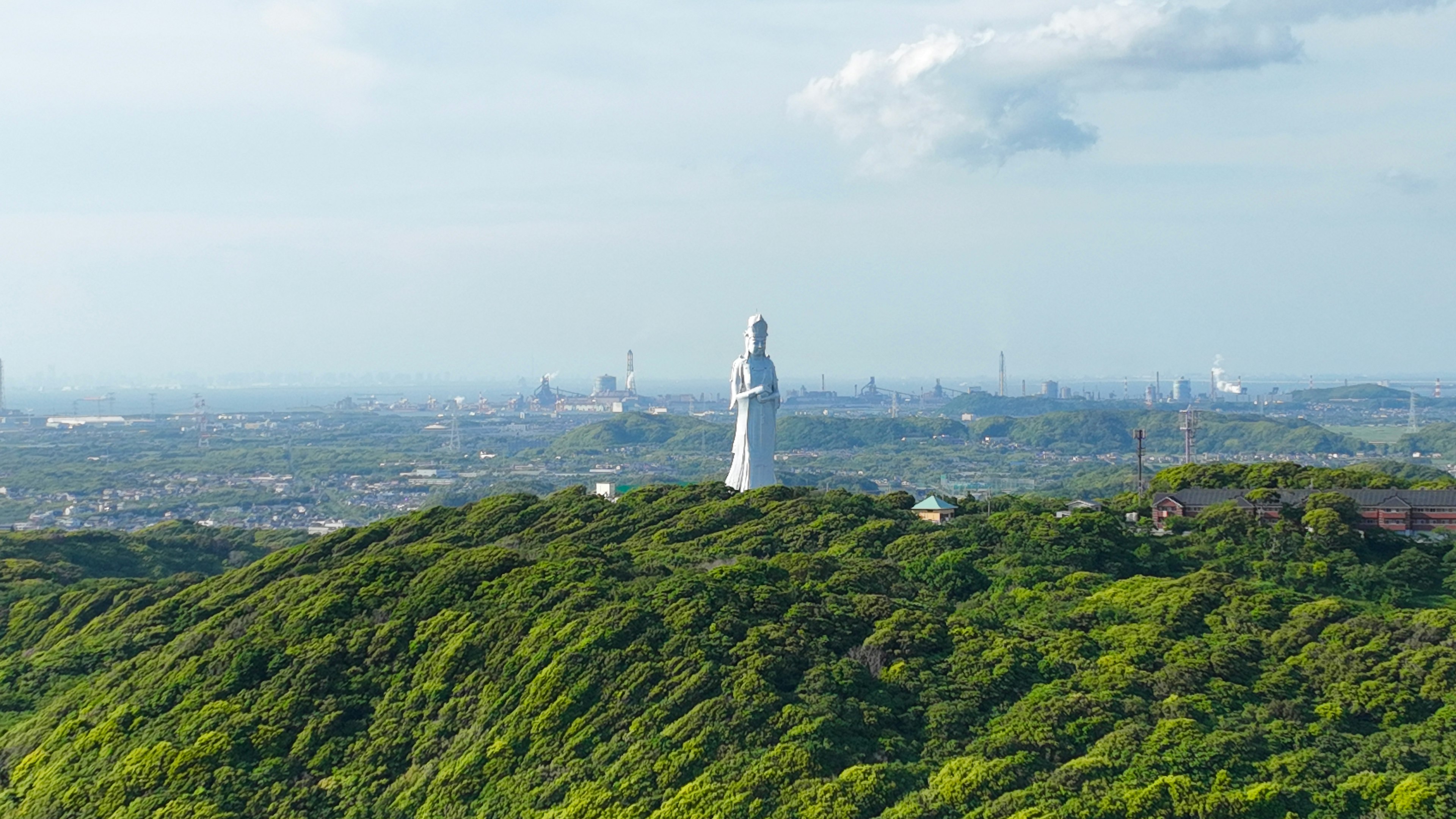 Patung putih di atas bukit hijau dengan cakrawala kota di kejauhan