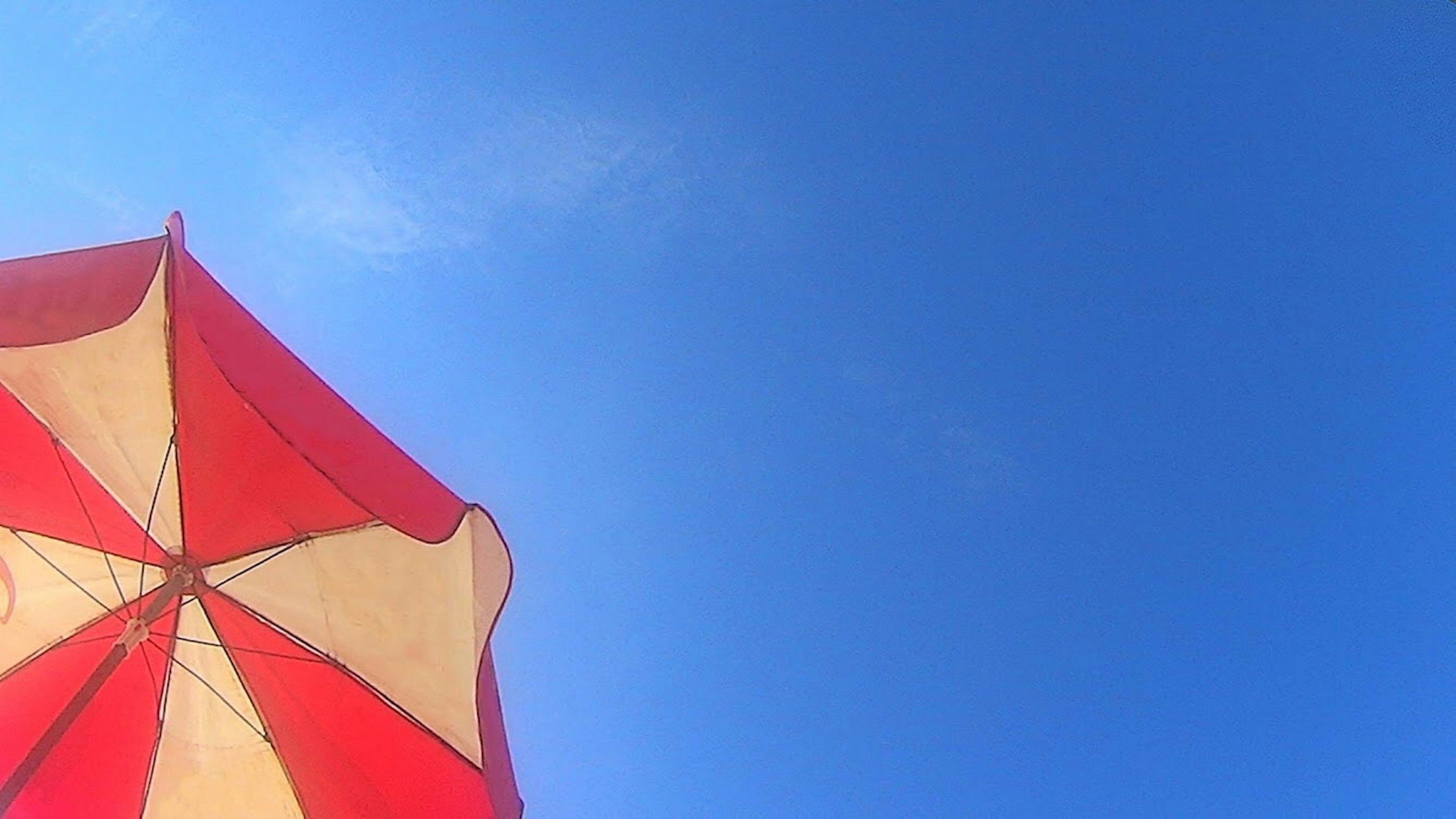 Red and white beach umbrella against a blue sky