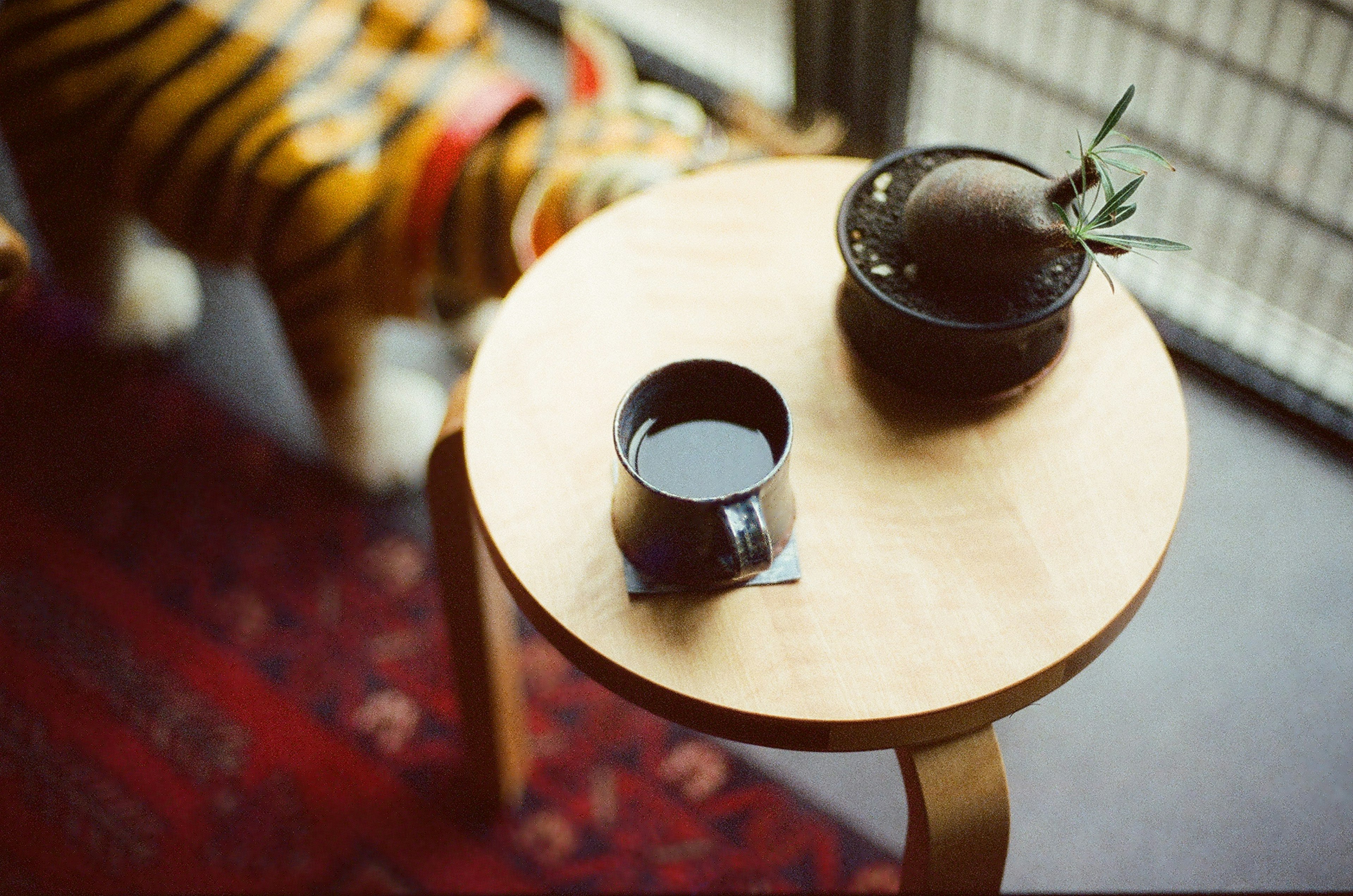 A wooden table featuring a black mug and a plant with a stuffed tiger seen nearby