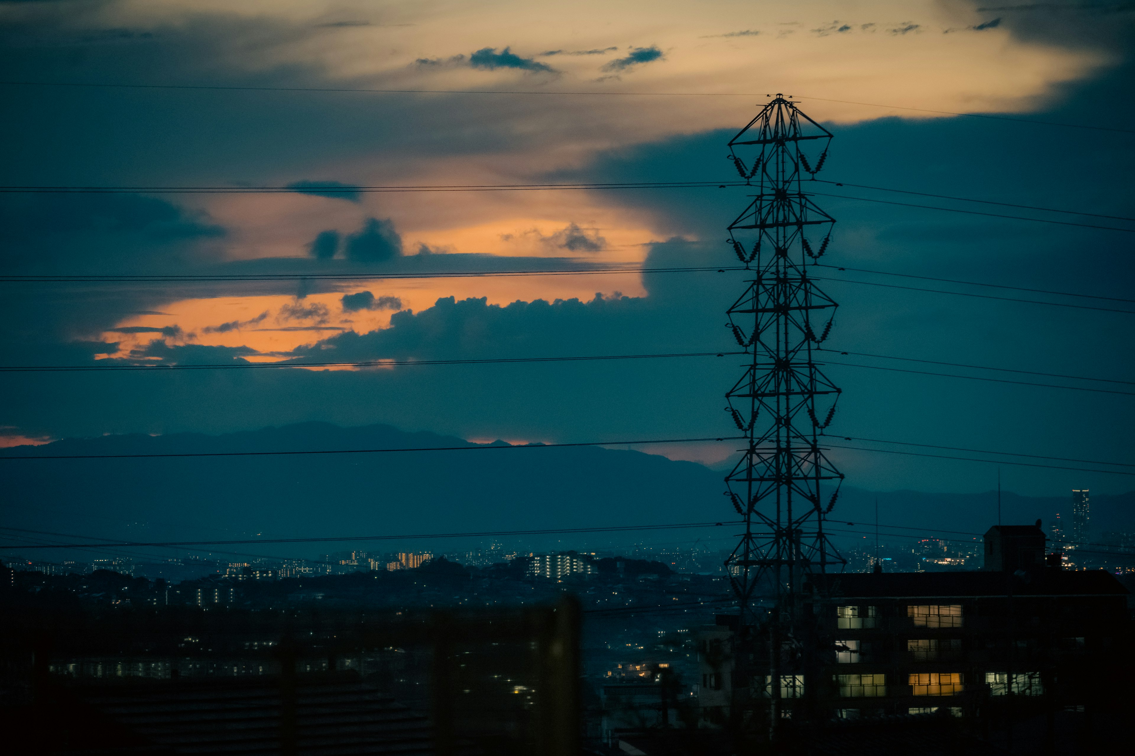 Städtische Landschaft bei Dämmerung mit einem Sendemast und fernen Bergen