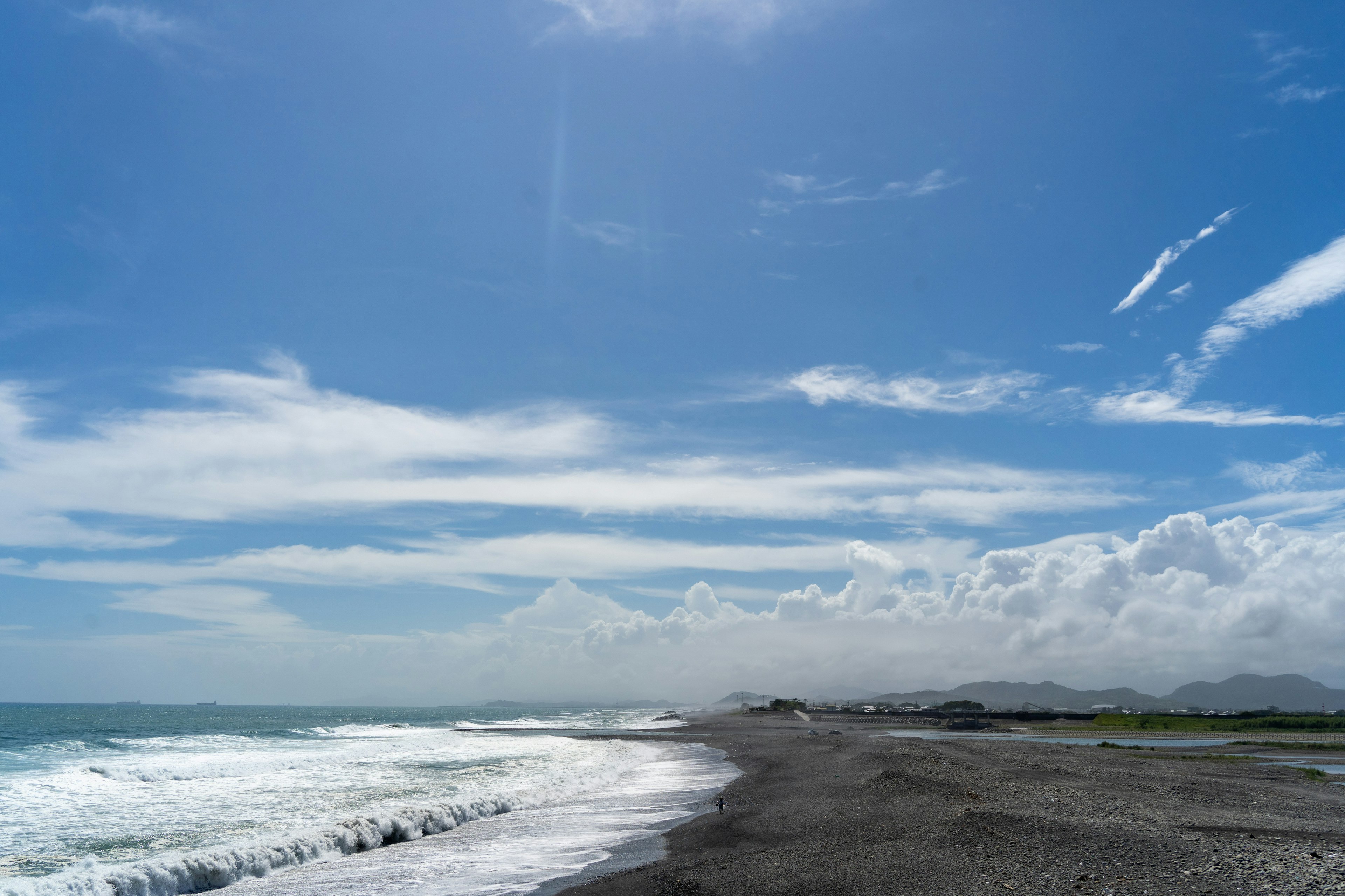 Pemandangan pantai dengan langit biru dan awan putih ombak menghantam pasir hitam