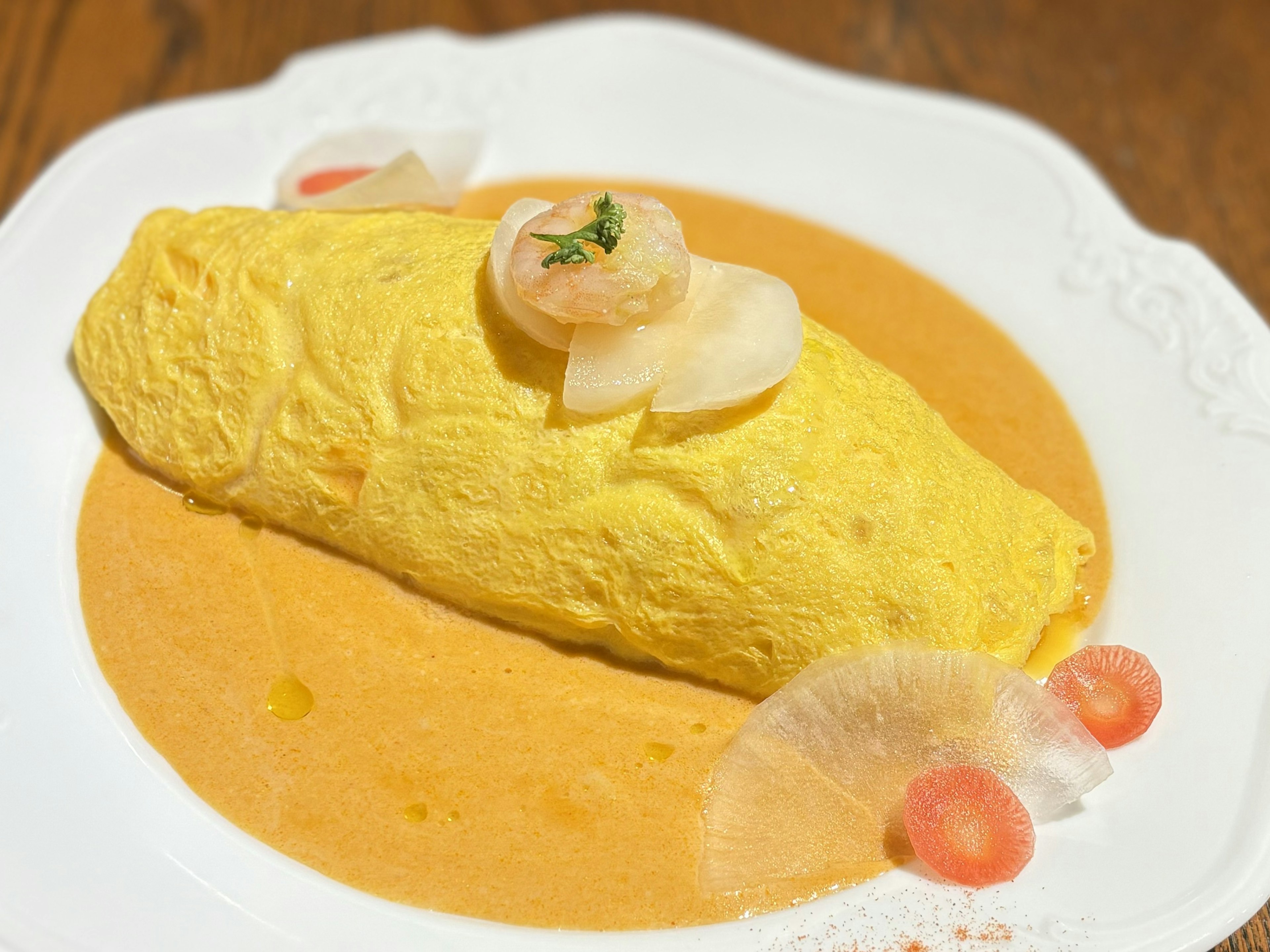 Creamy omelette rice on a bed of orange sauce garnished with shrimp and vegetables