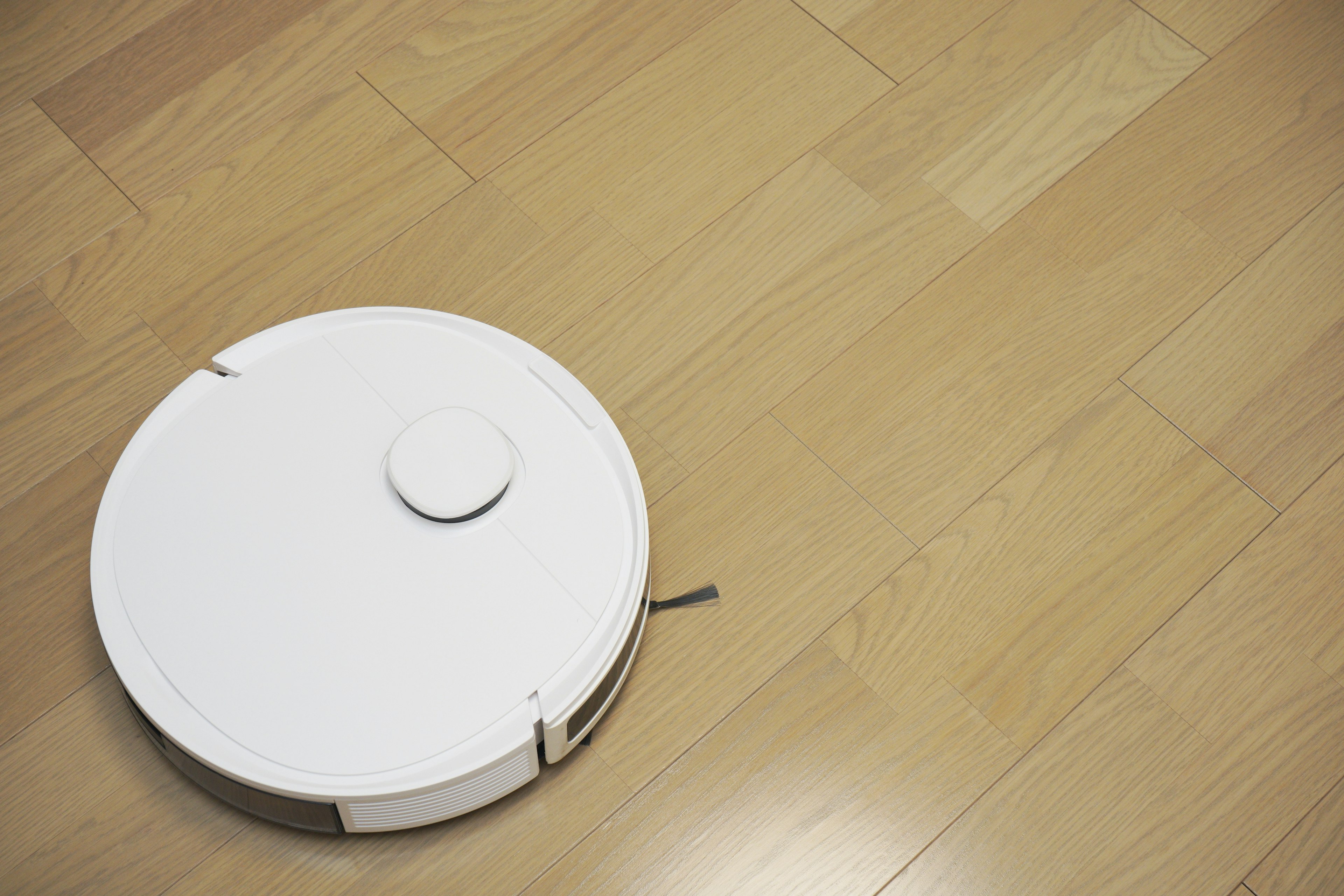 A white robotic vacuum cleaner on a wooden floor