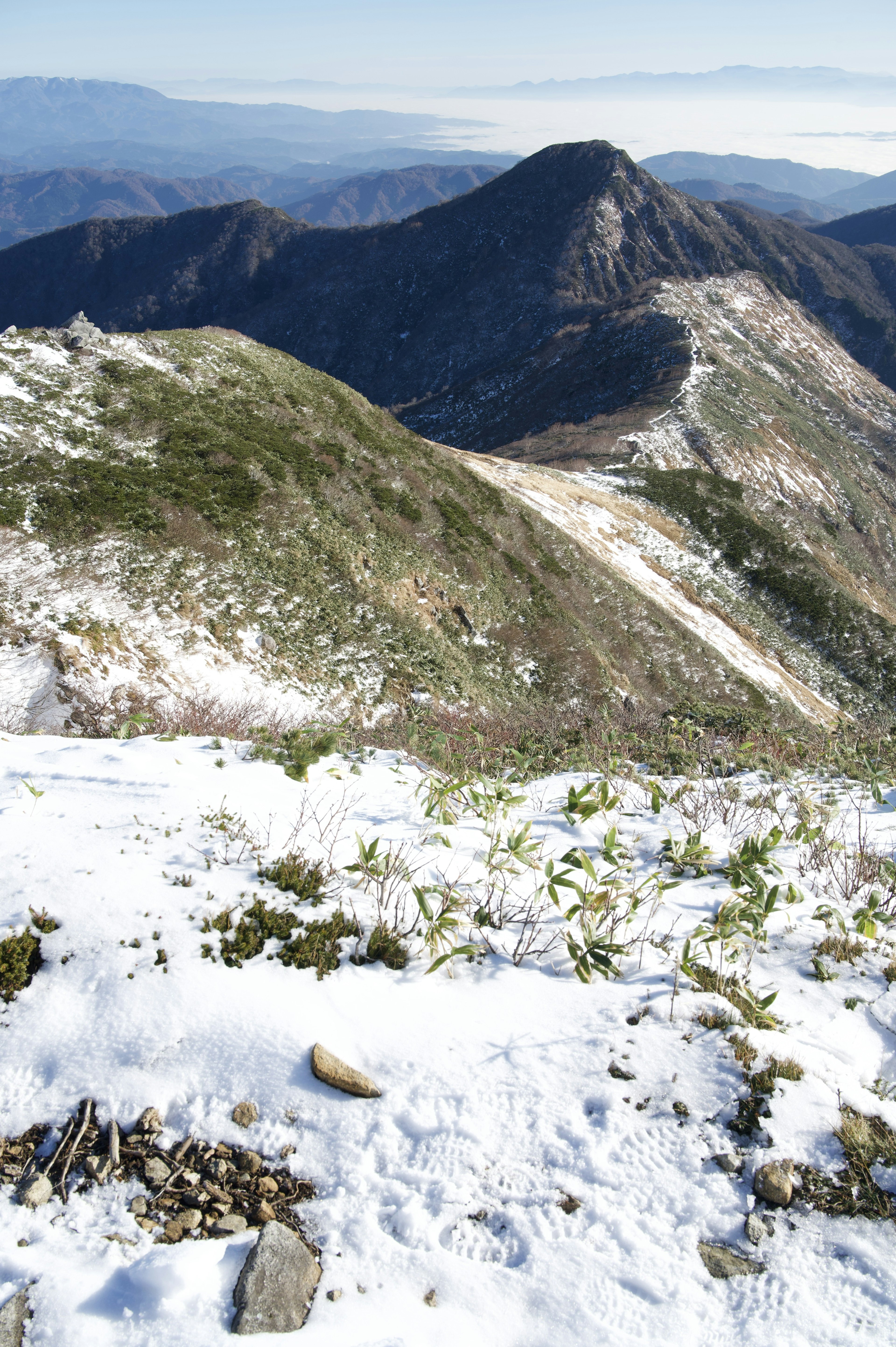 雪に覆われた山の斜面と遠くの山々が見える風景