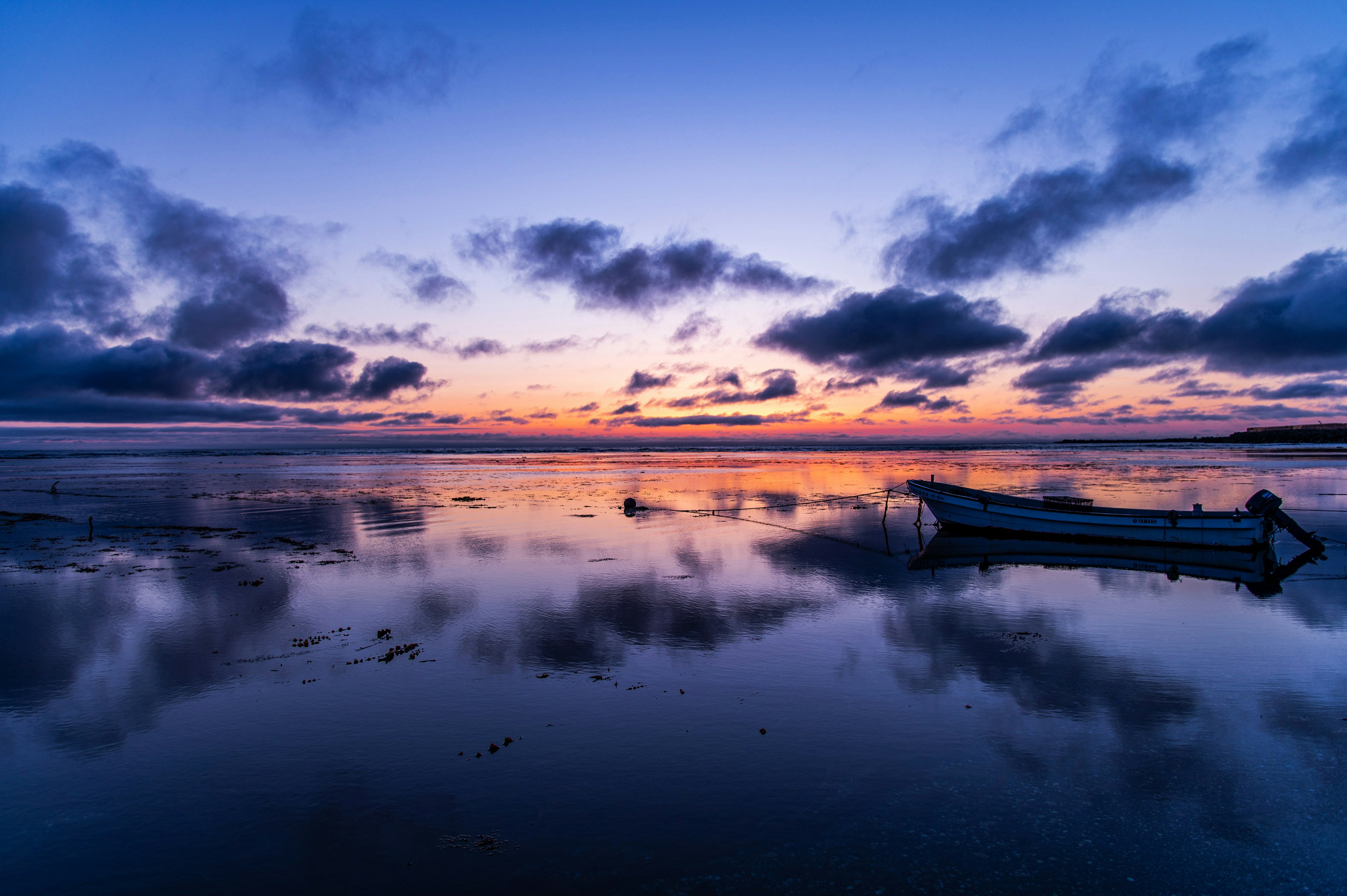 Acqua calma che riflette il tramonto e le nuvole con una barca ormeggiata a riva