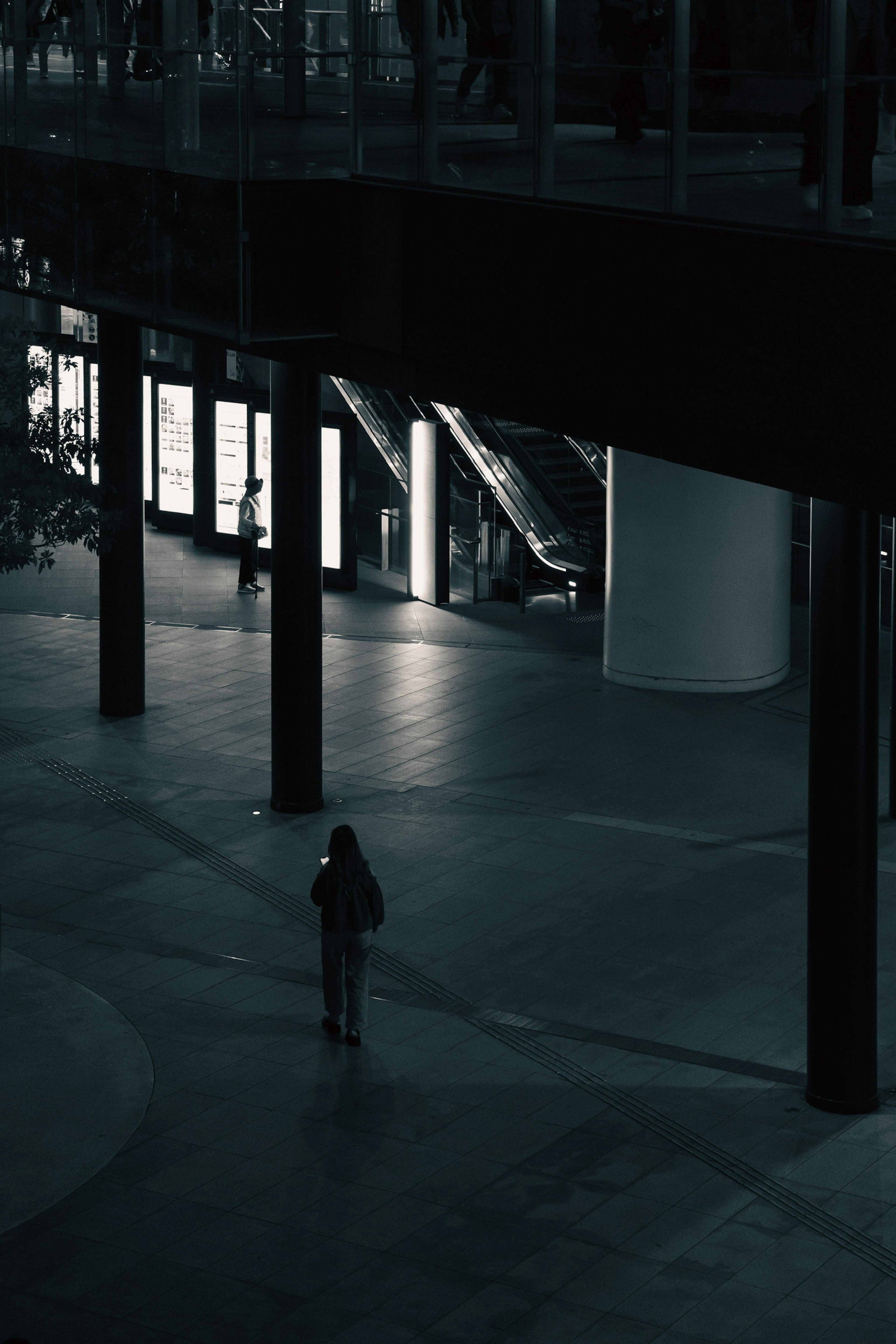 Silhouette d'une personne marchant seule dans un espace intérieur faiblement éclairé fenêtres lumineuses et escaliers visibles