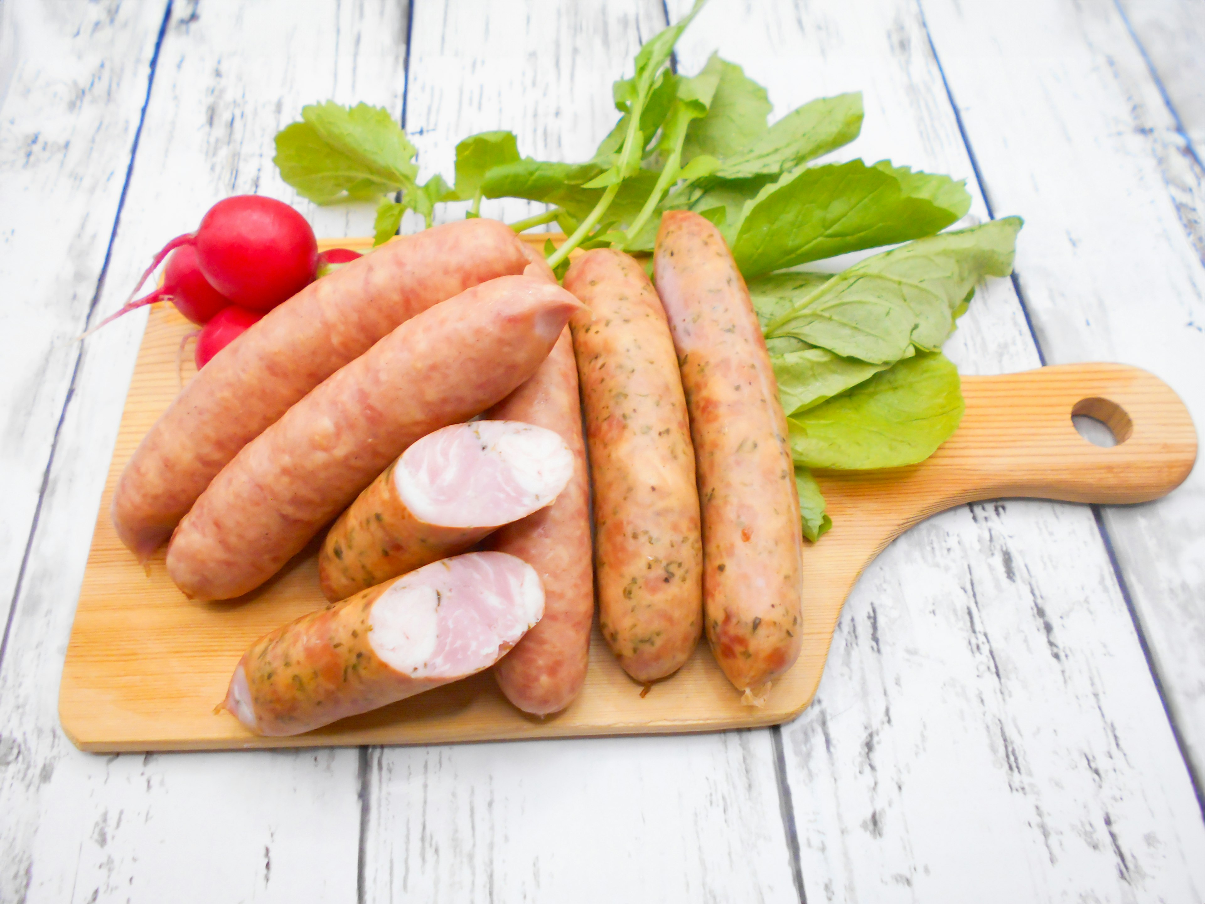 Salchichas en una tabla de madera con rábanos frescos y verduras de hoja