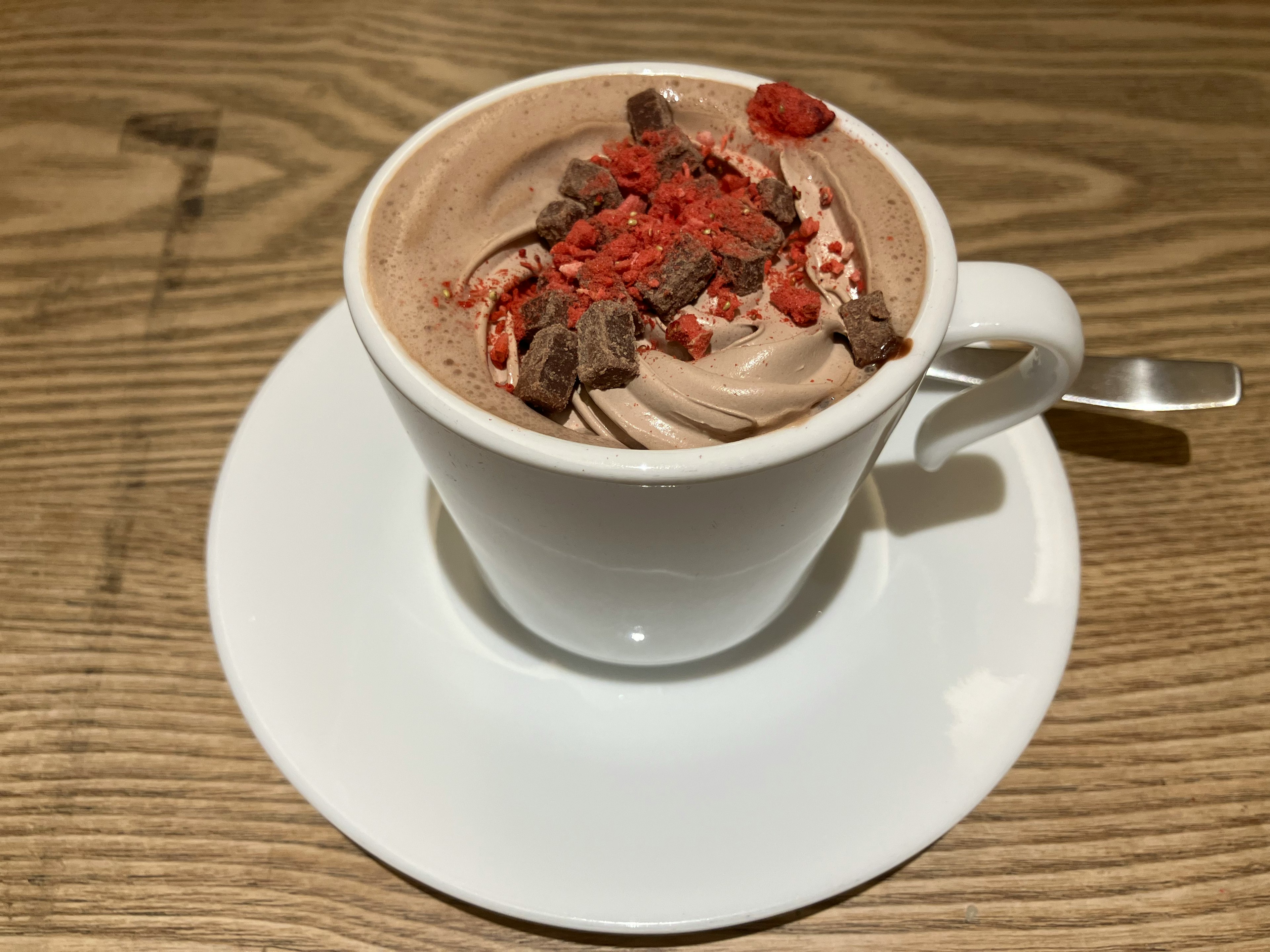 Creamy chocolate dessert in a white cup topped with chocolate shavings and strawberry pieces