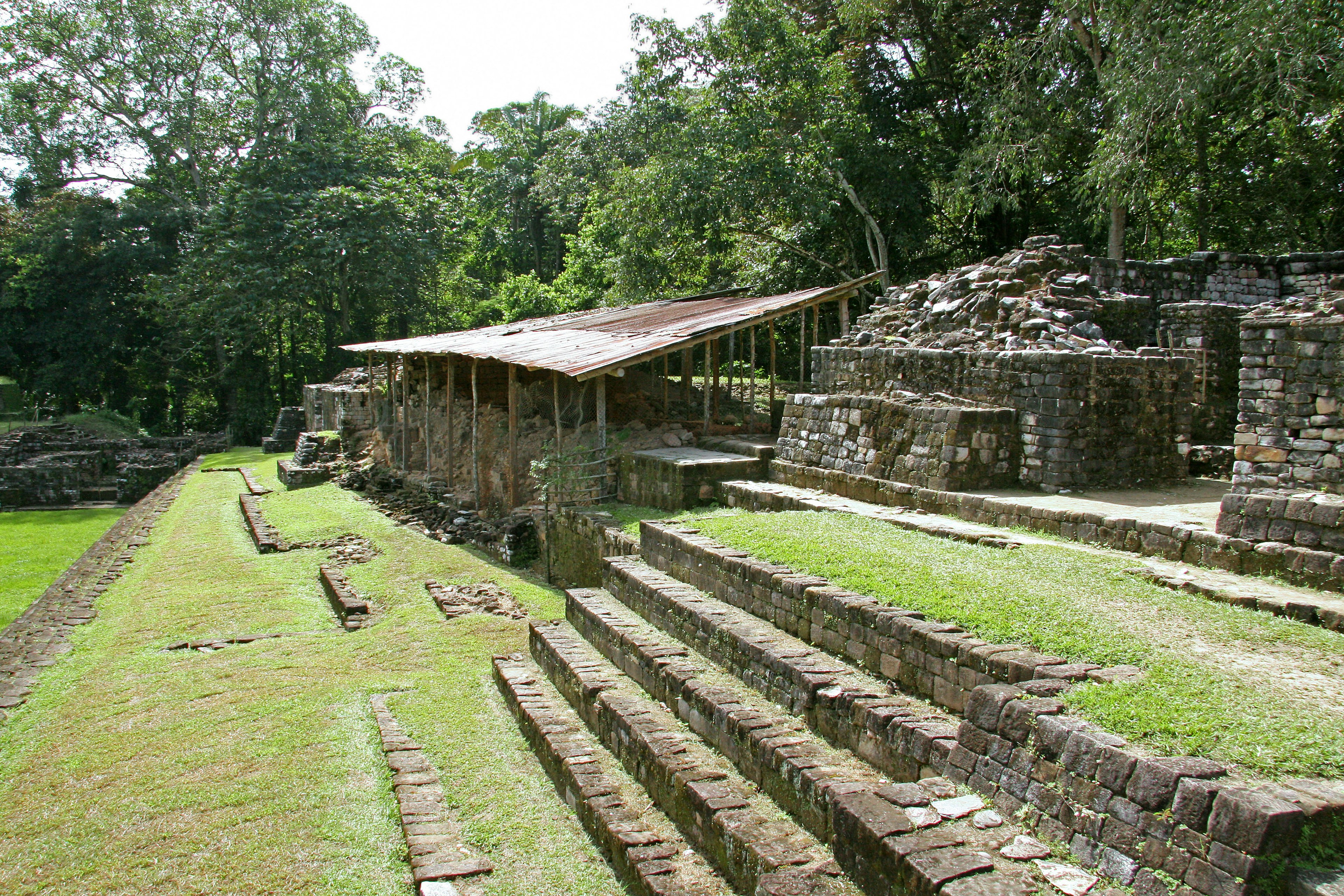 Ruinas antiguas con escaleras de piedra y una estructura cubierta en un entorno verde