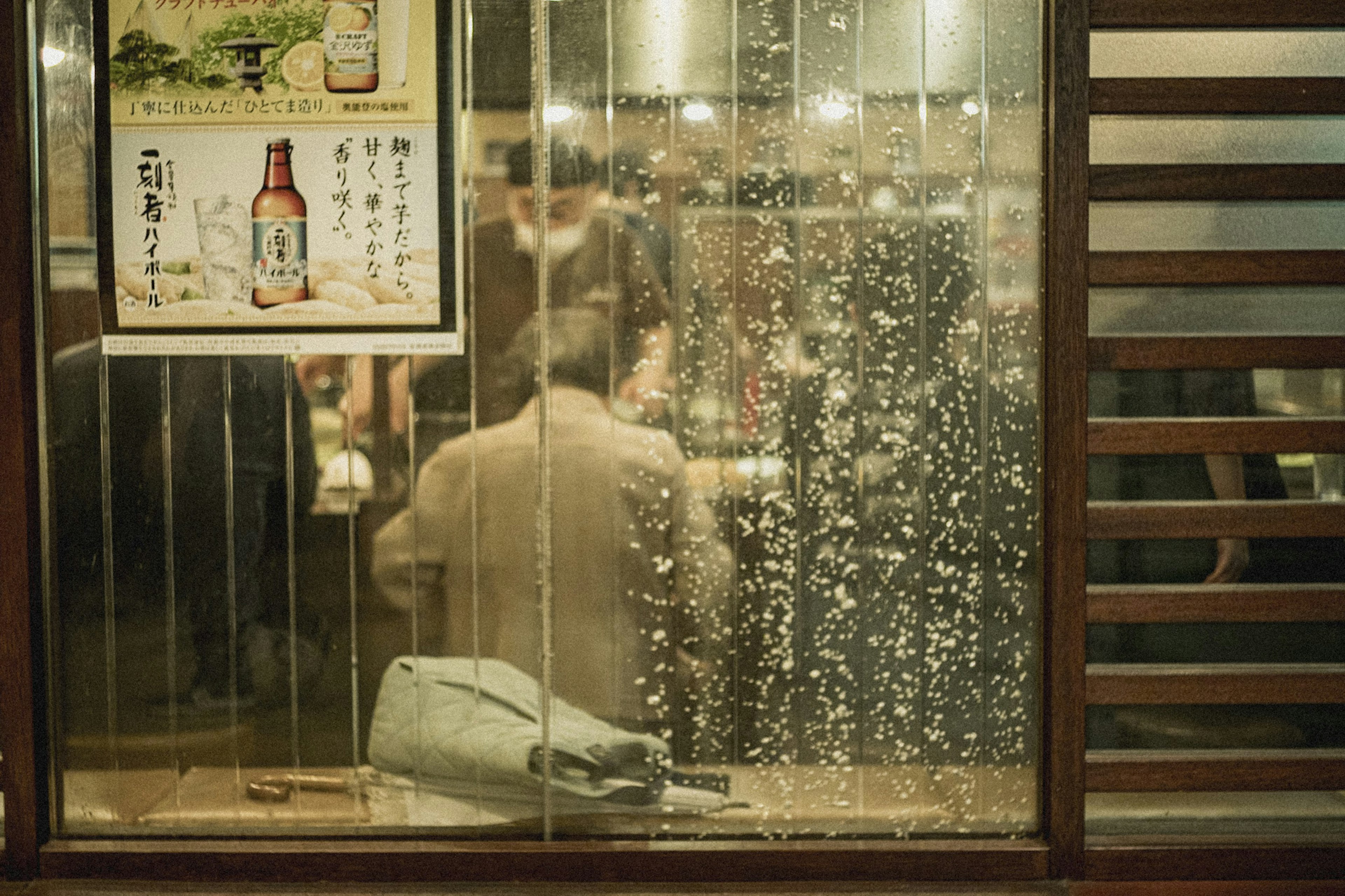 雨に濡れたガラス越しの飲食店の内部の様子と人々