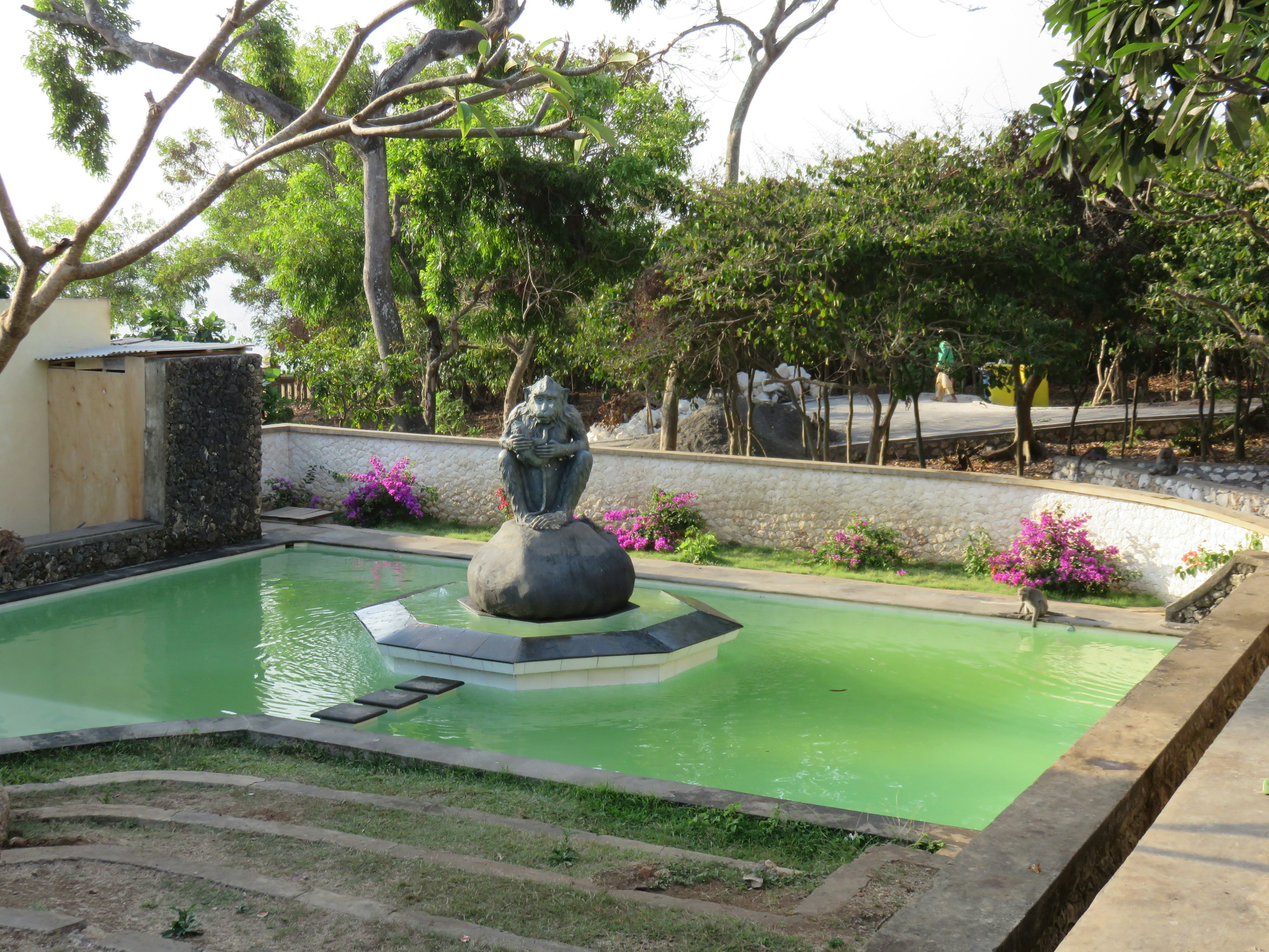 Escena de jardín con una escultura de piedra en un estanque verde rodeado de flores