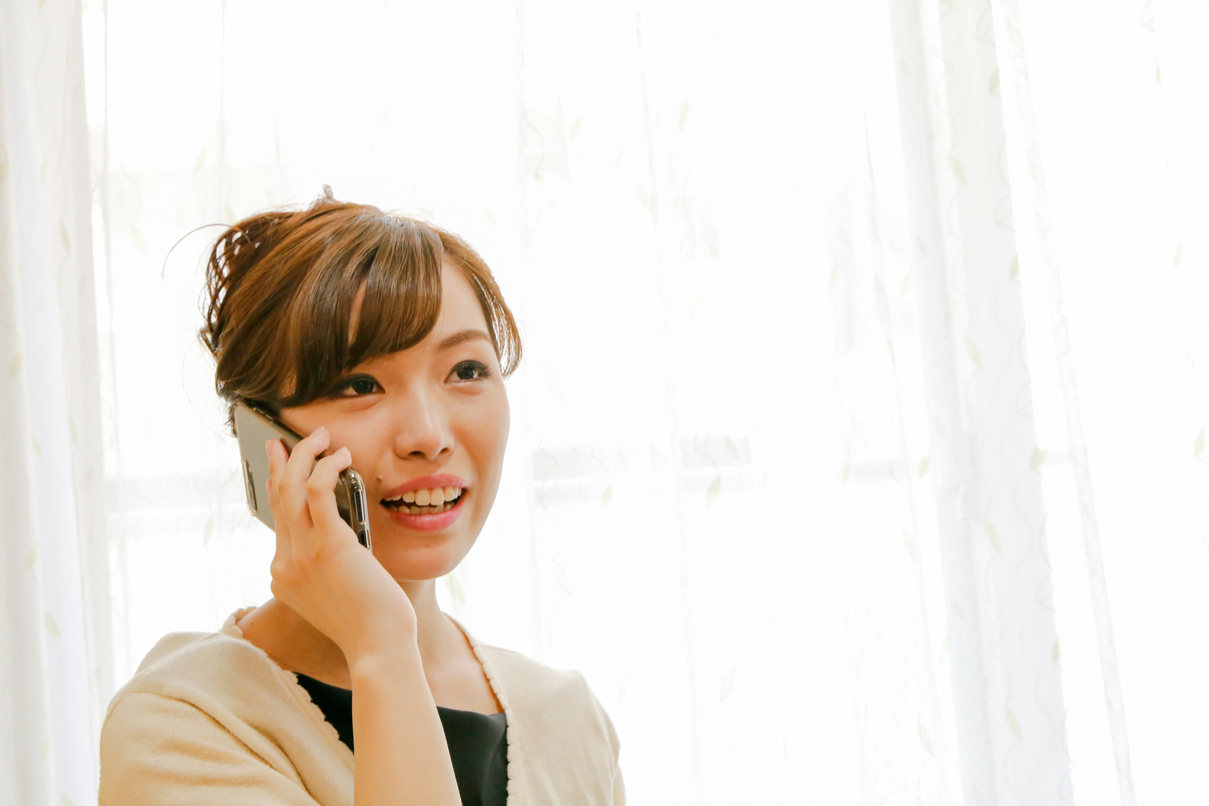 A smiling woman talking on the phone in front of a bright window