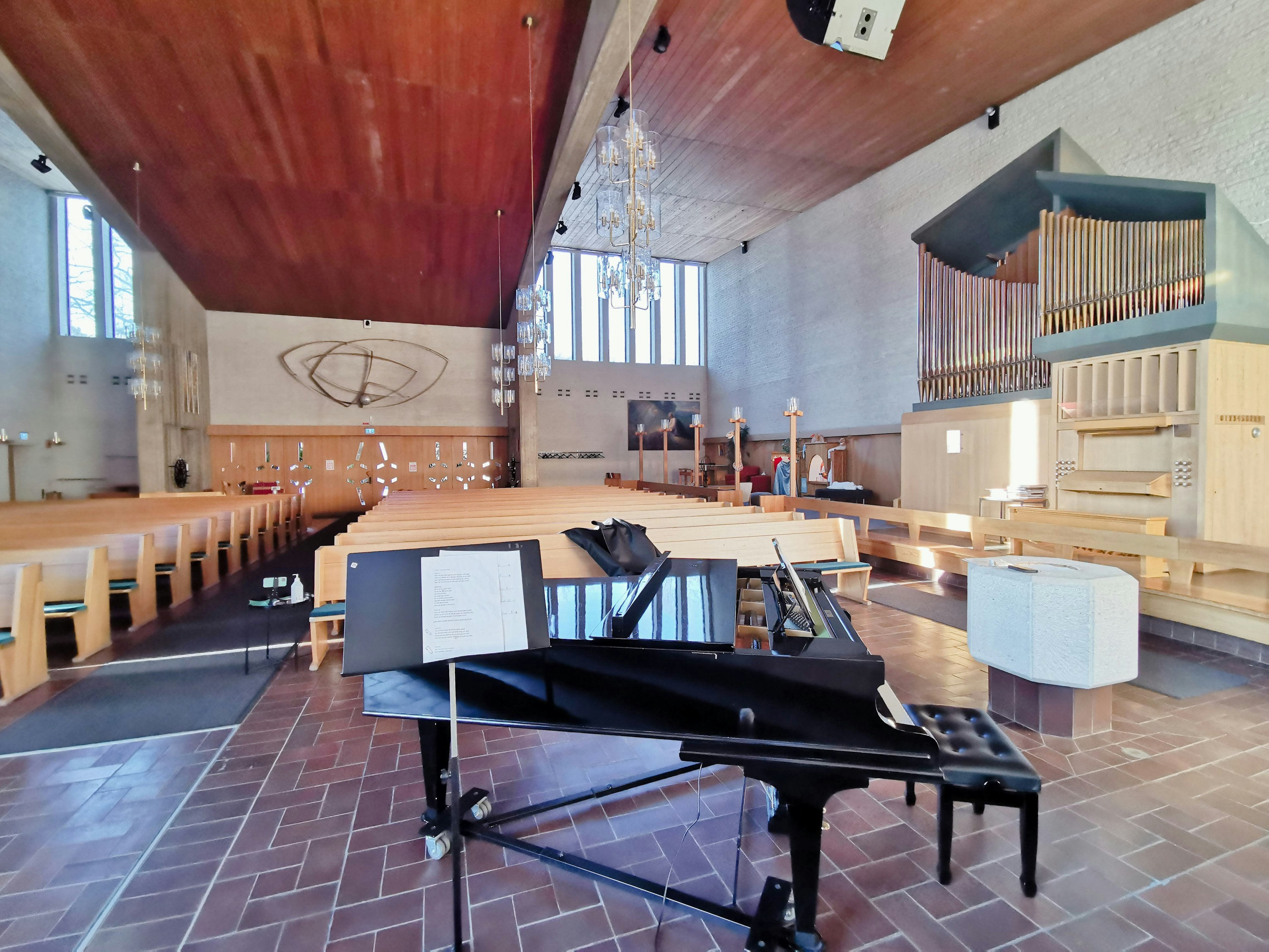 Interior of a church with a bright wooden ceiling featuring a grand piano and an organ