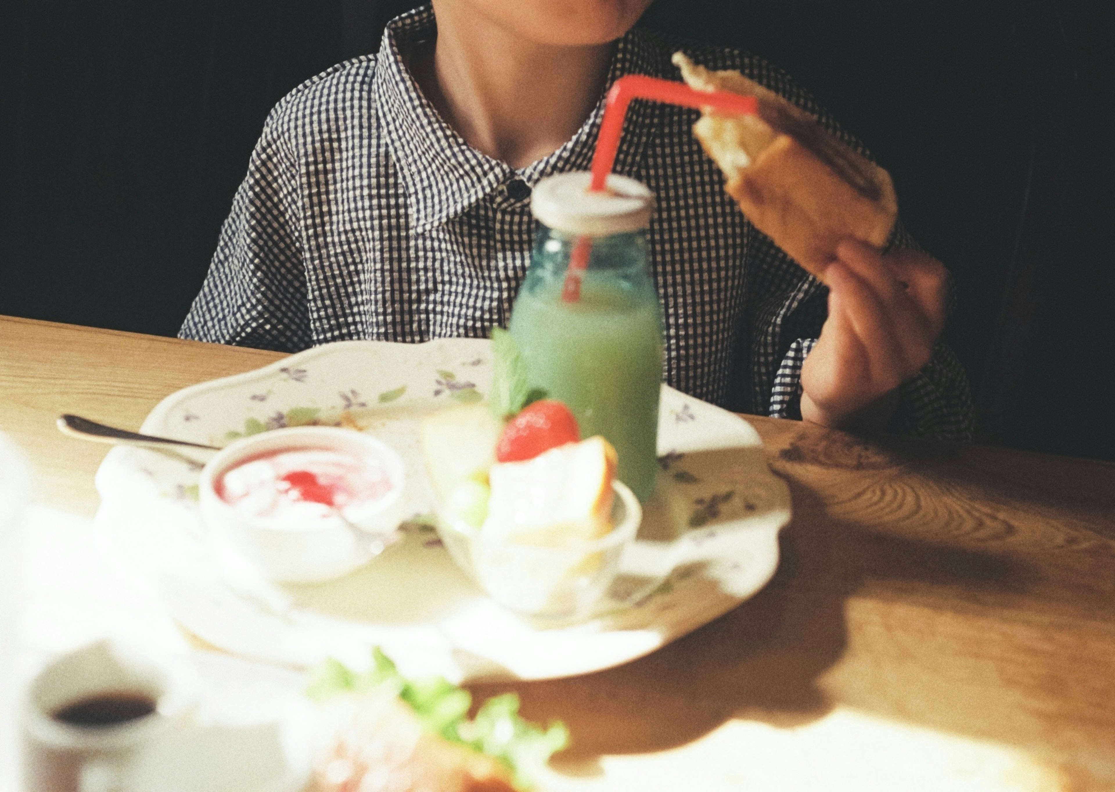 Niño sosteniendo un sándwich y una bebida verde con una pajita sobre una mesa