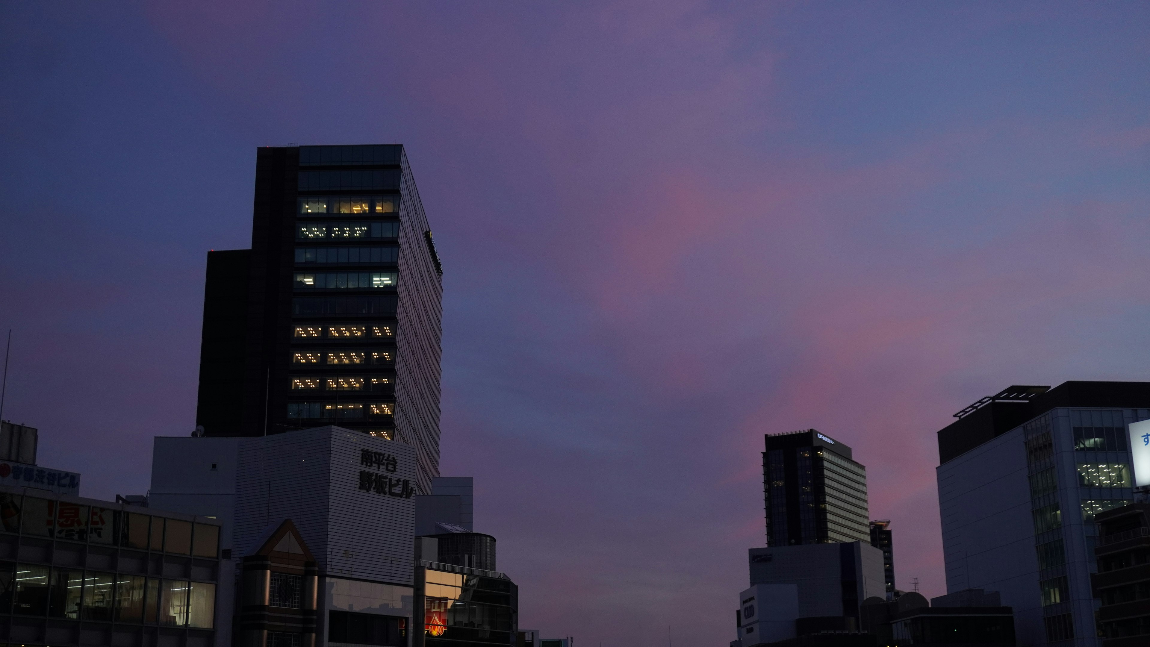 Silueta de edificios contra un cielo al atardecer con nubes moradas suaves