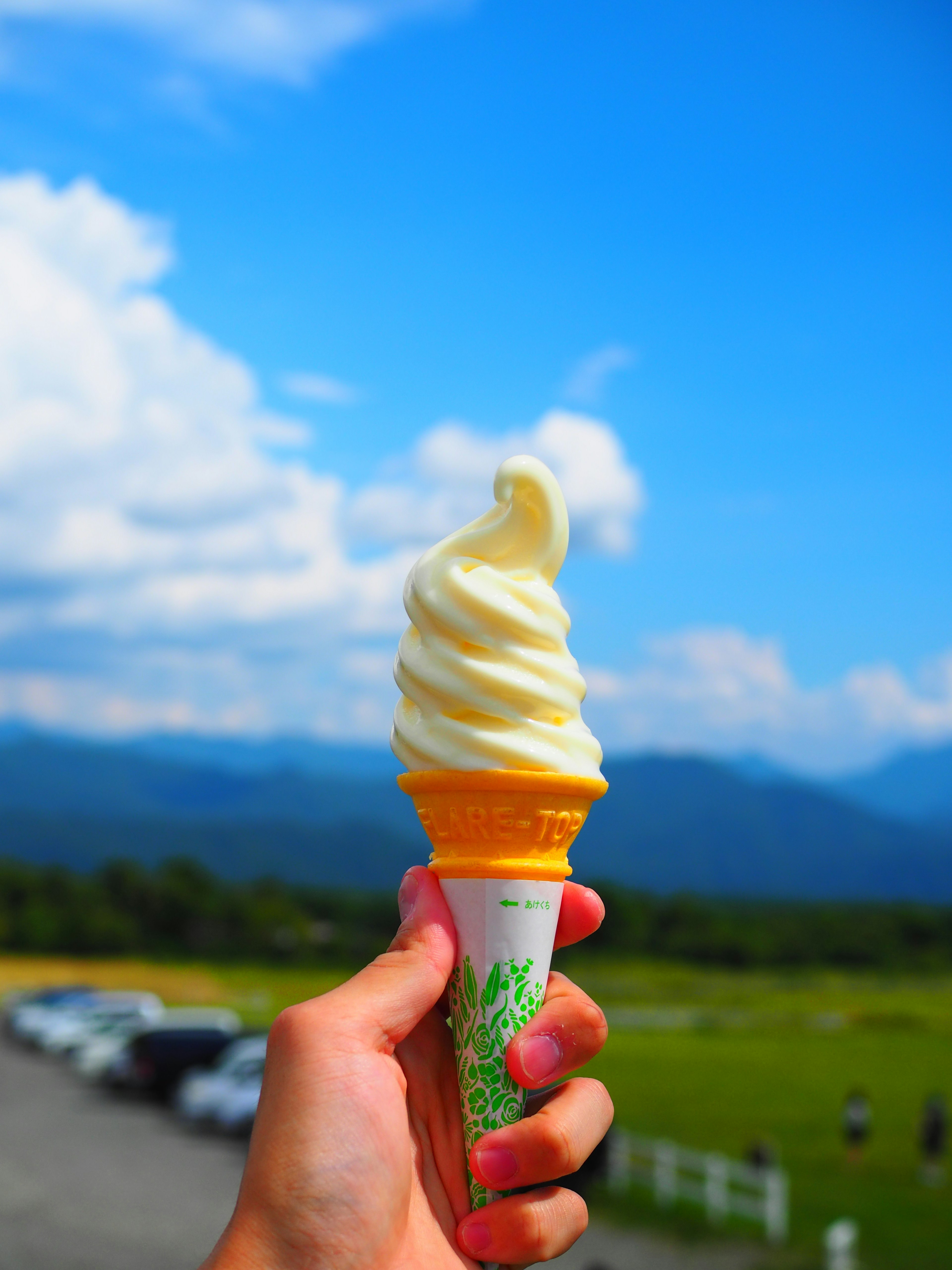 Hand holding a soft-serve ice cream cone against a blue sky