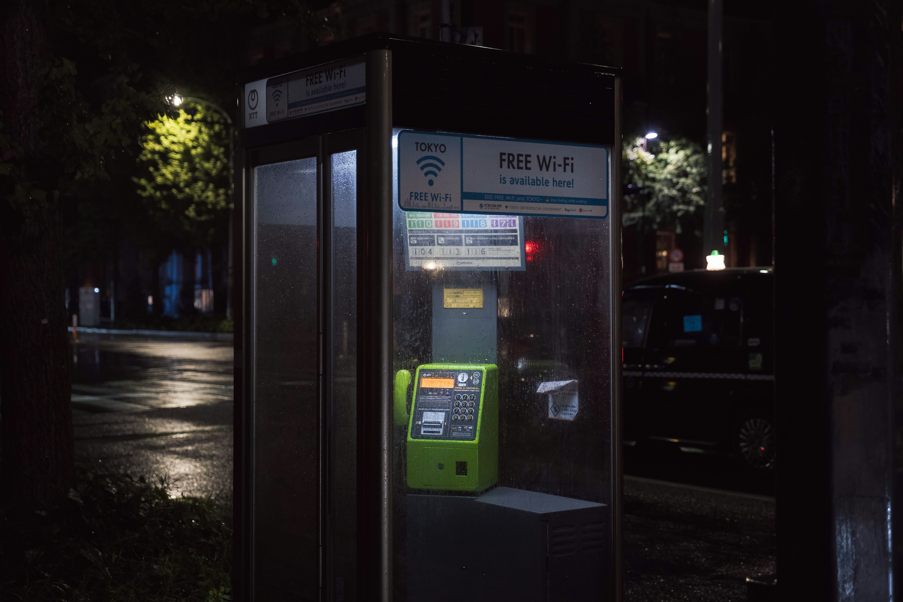 A phone booth with a green payphone on a street corner at night