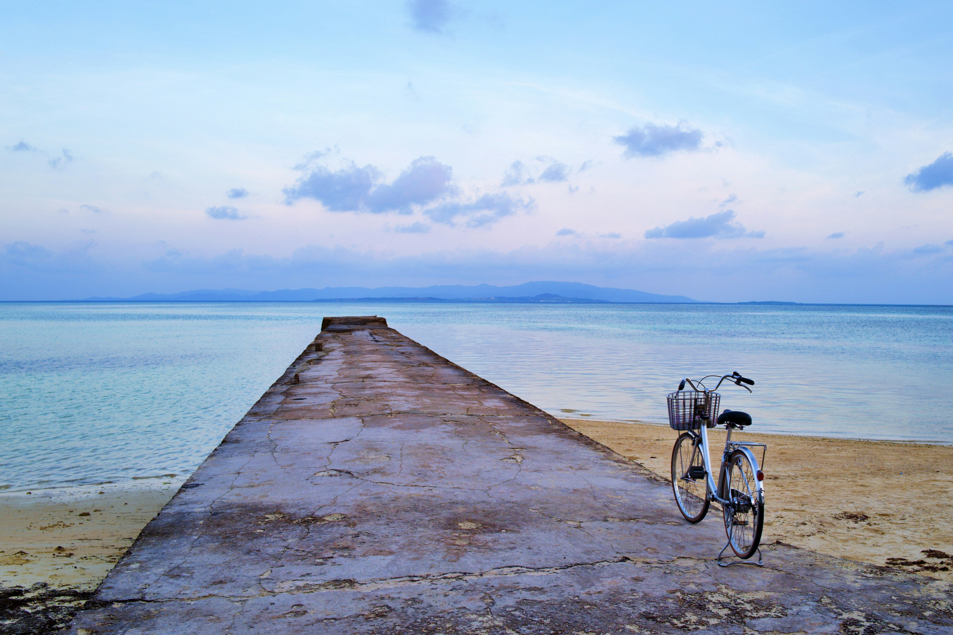 Sebuah sepeda di dermaga yang membentang ke laut tenang di bawah langit biru