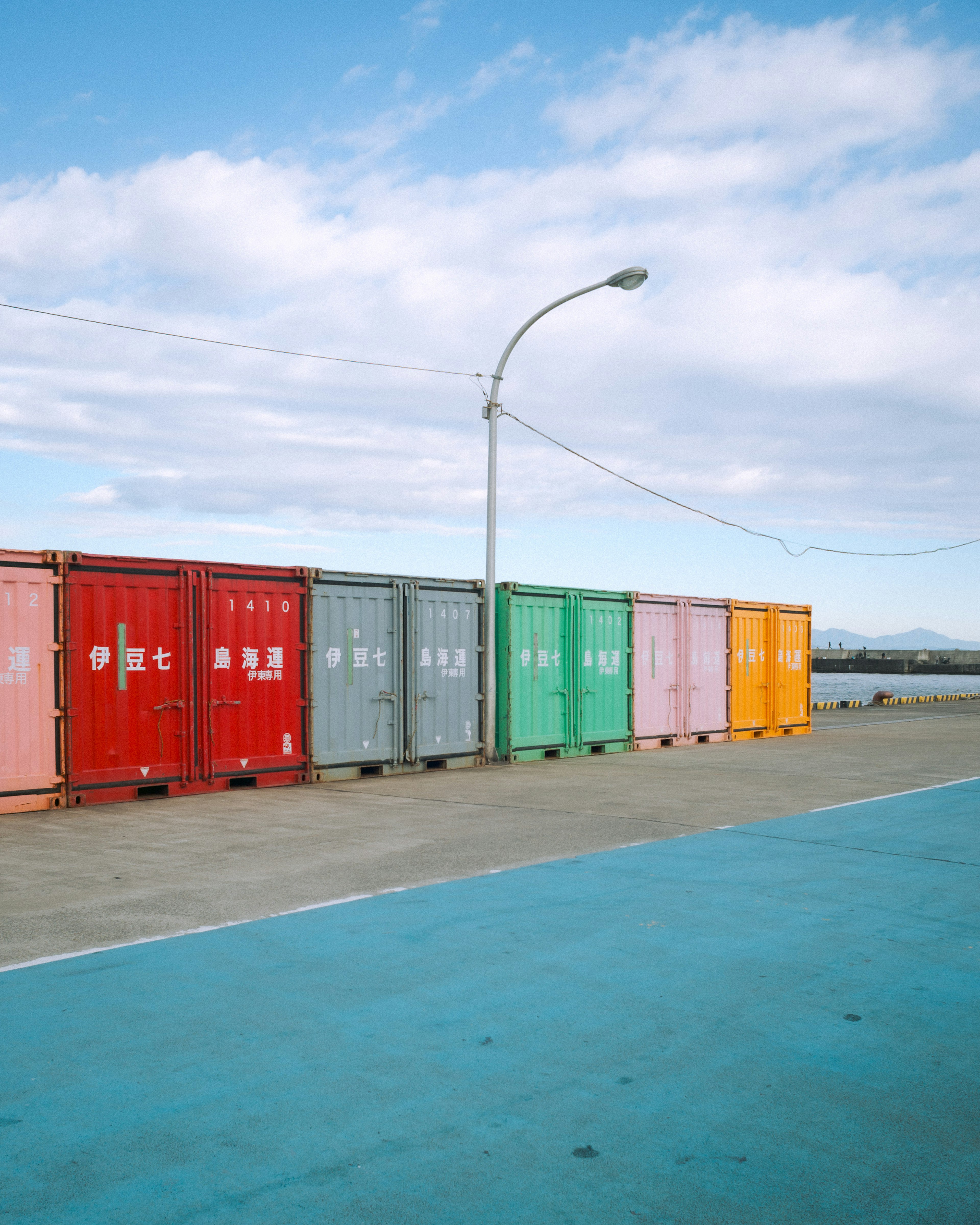 Contenedores coloridos alineados en un puerto con pavimento azul y cielo brillante