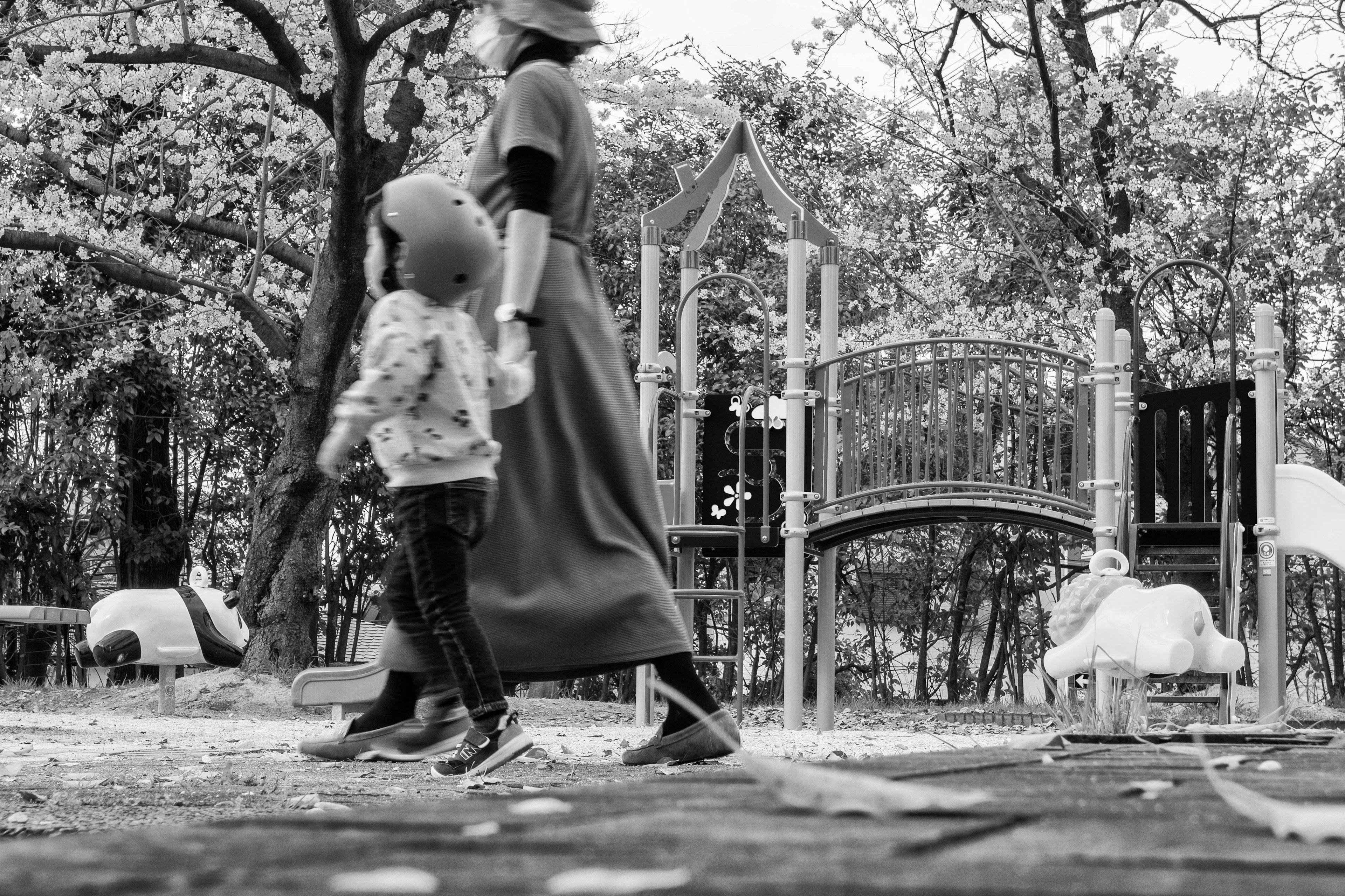 Schwarzweißfoto einer Mutter und eines Kindes, die in der Nähe von Spielgeräten in einem Park gehen