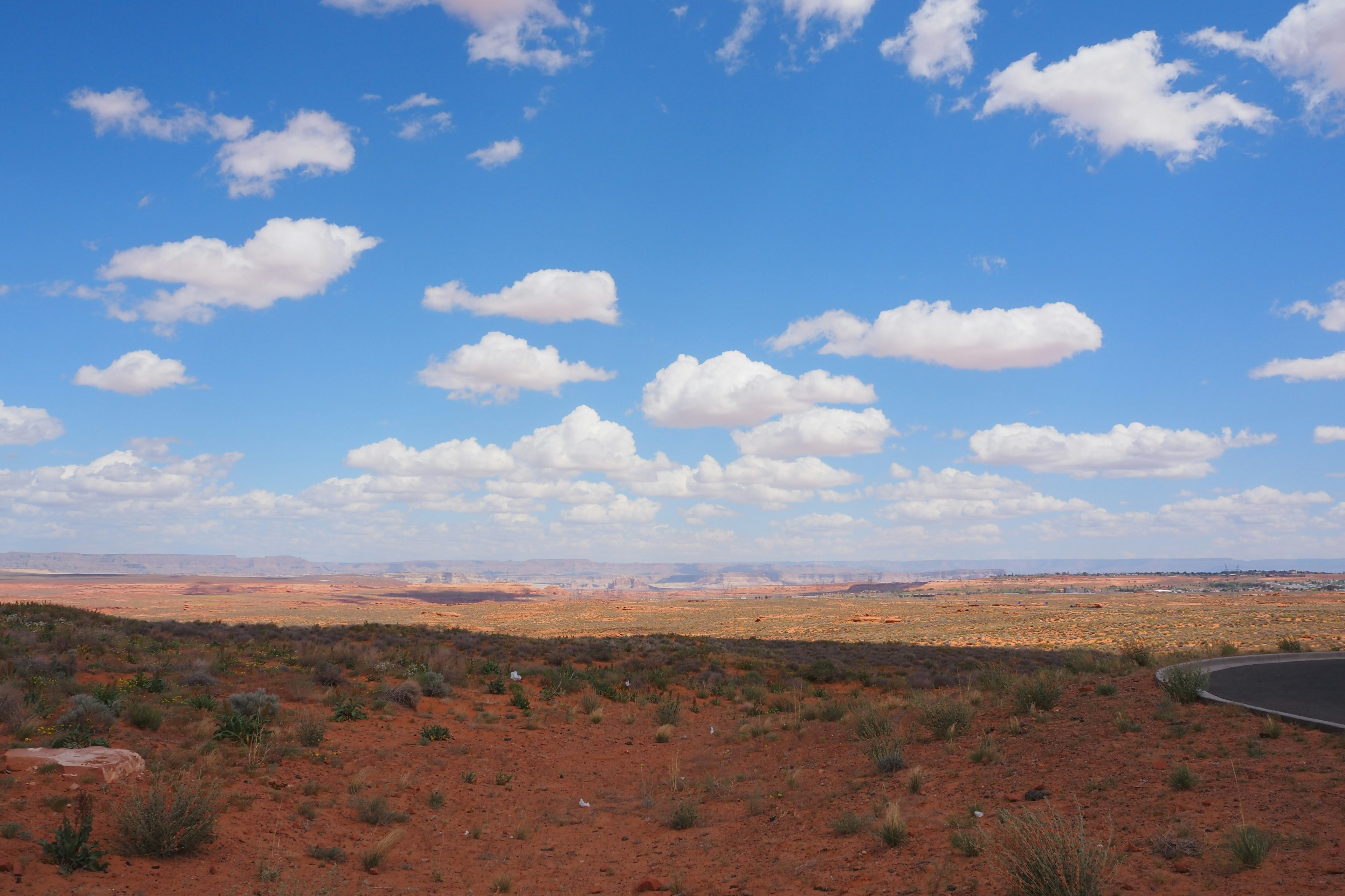 Expansive red desert landscape under a blue sky with white clouds