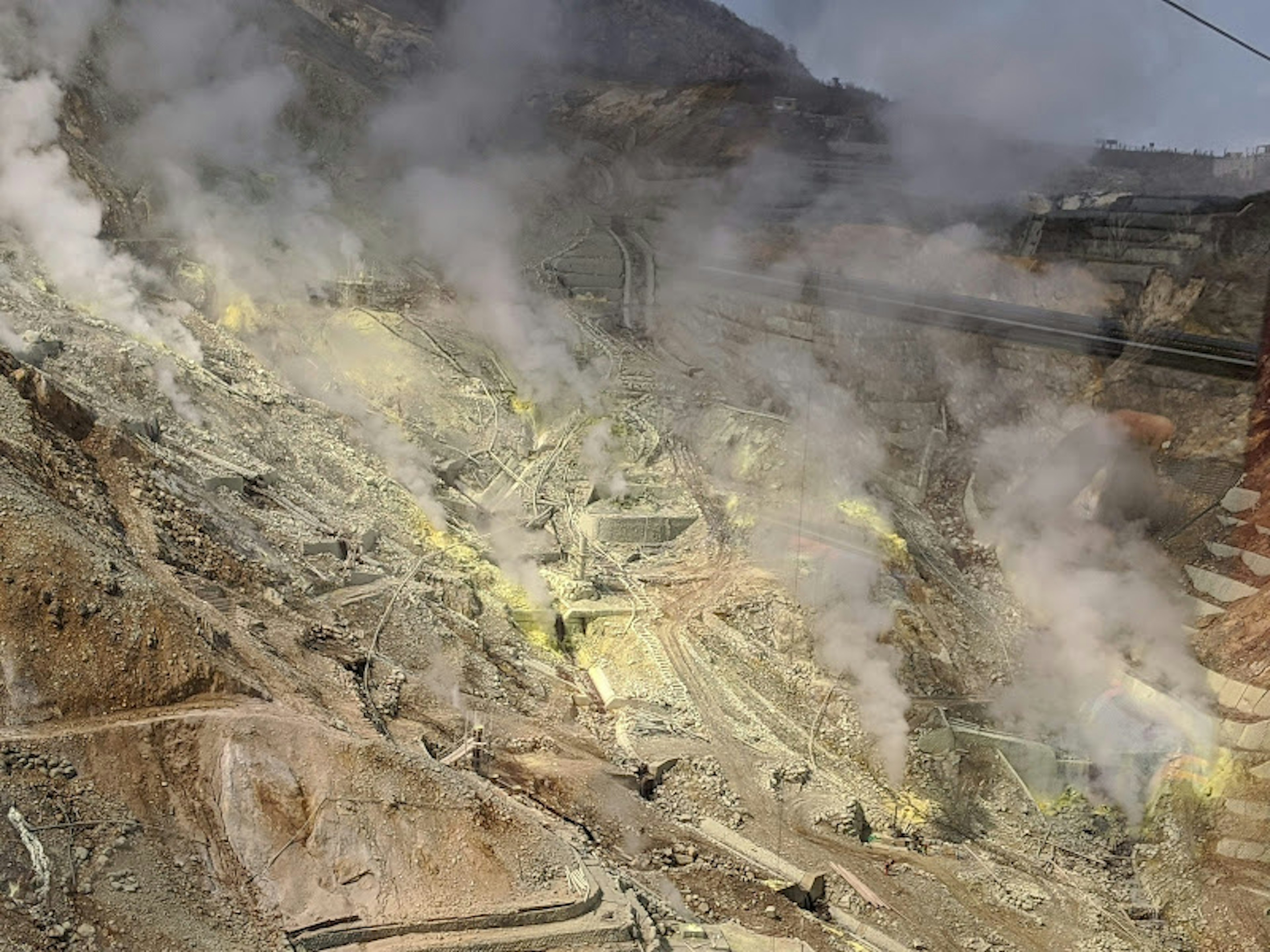 Workers on a sulfur-emitting mountainside with steam and yellow minerals