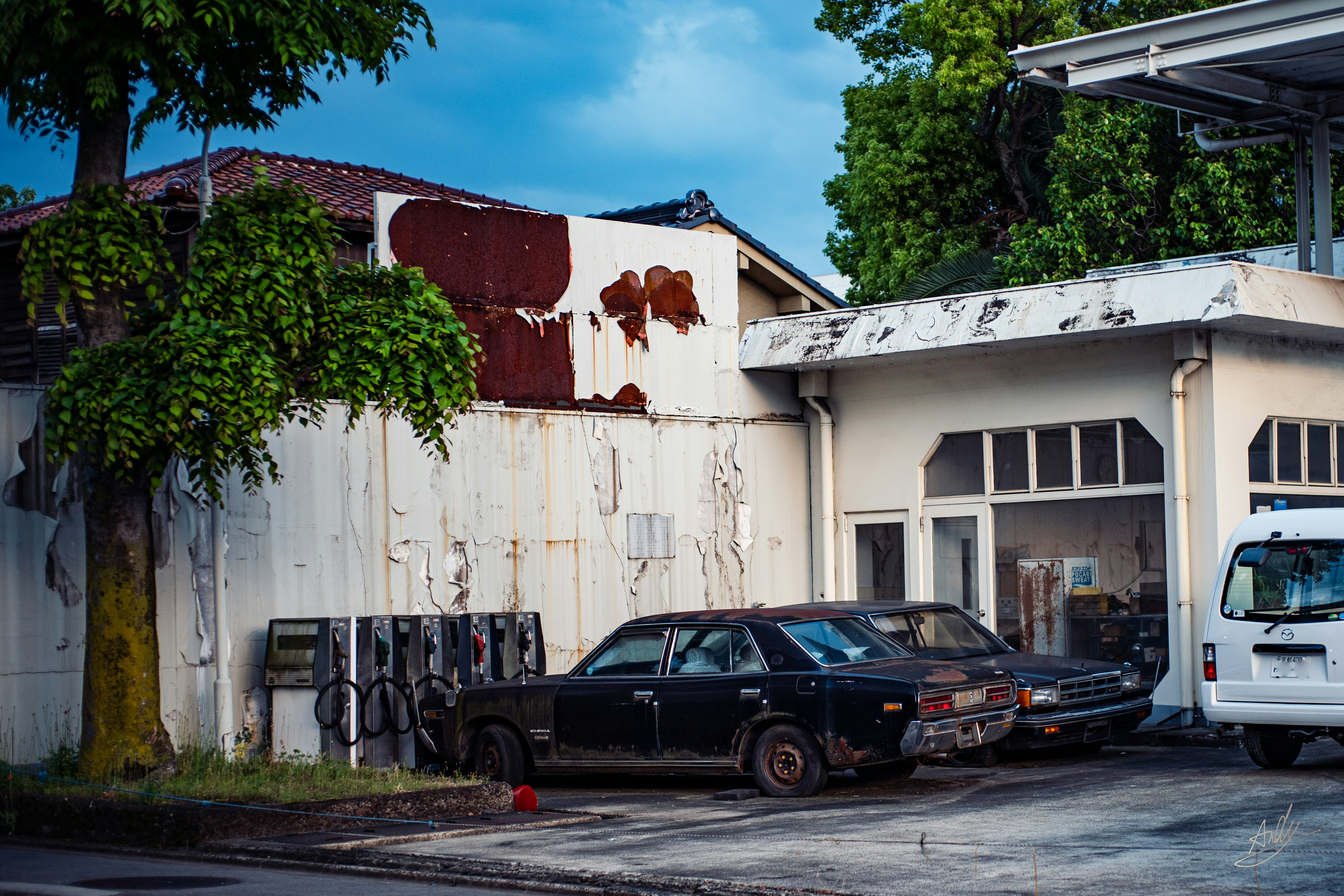 Voiture noire abandonnée à côté d'un bâtiment usé et d'arbres