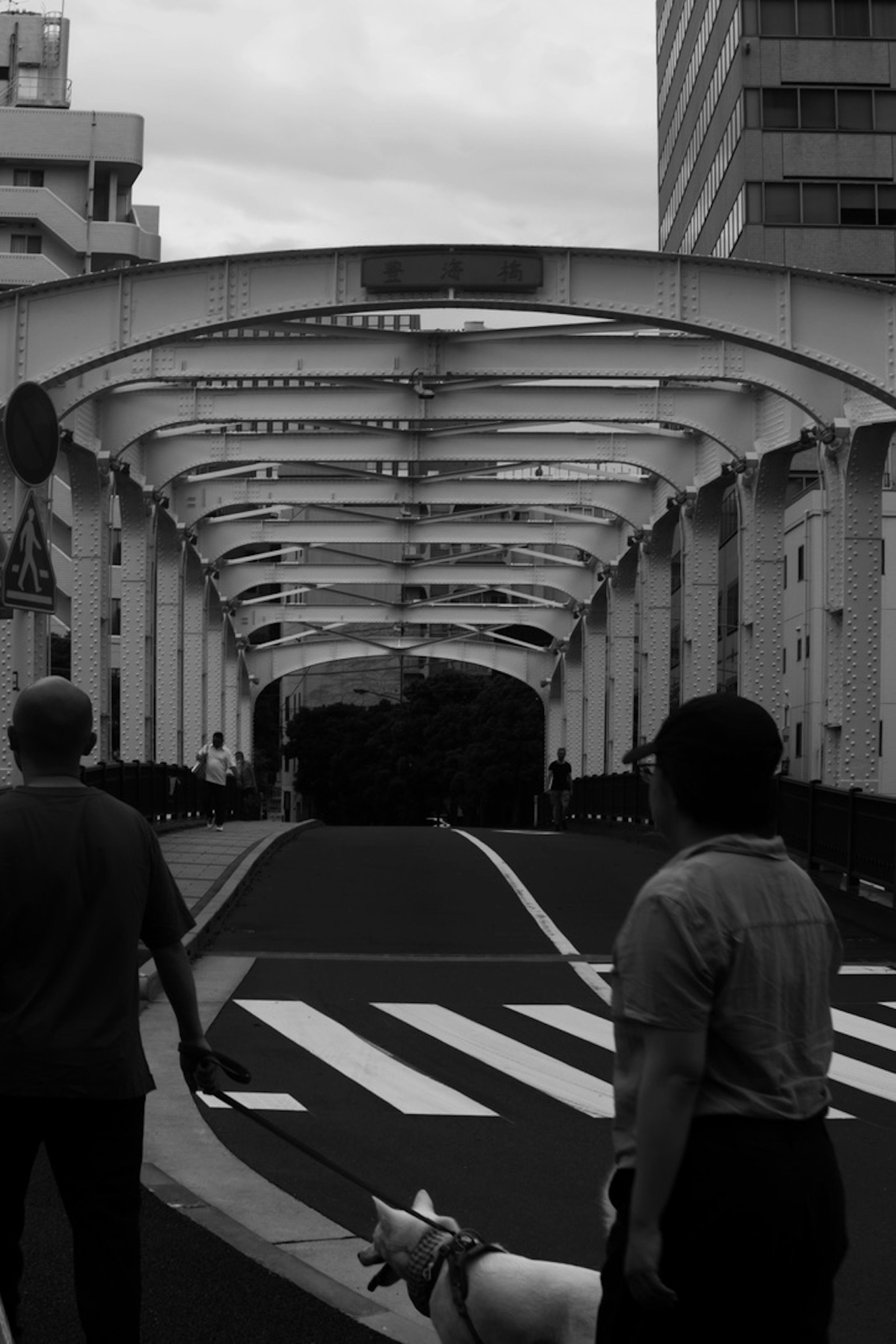 Two men walking under an archway bridge in a black and white urban setting