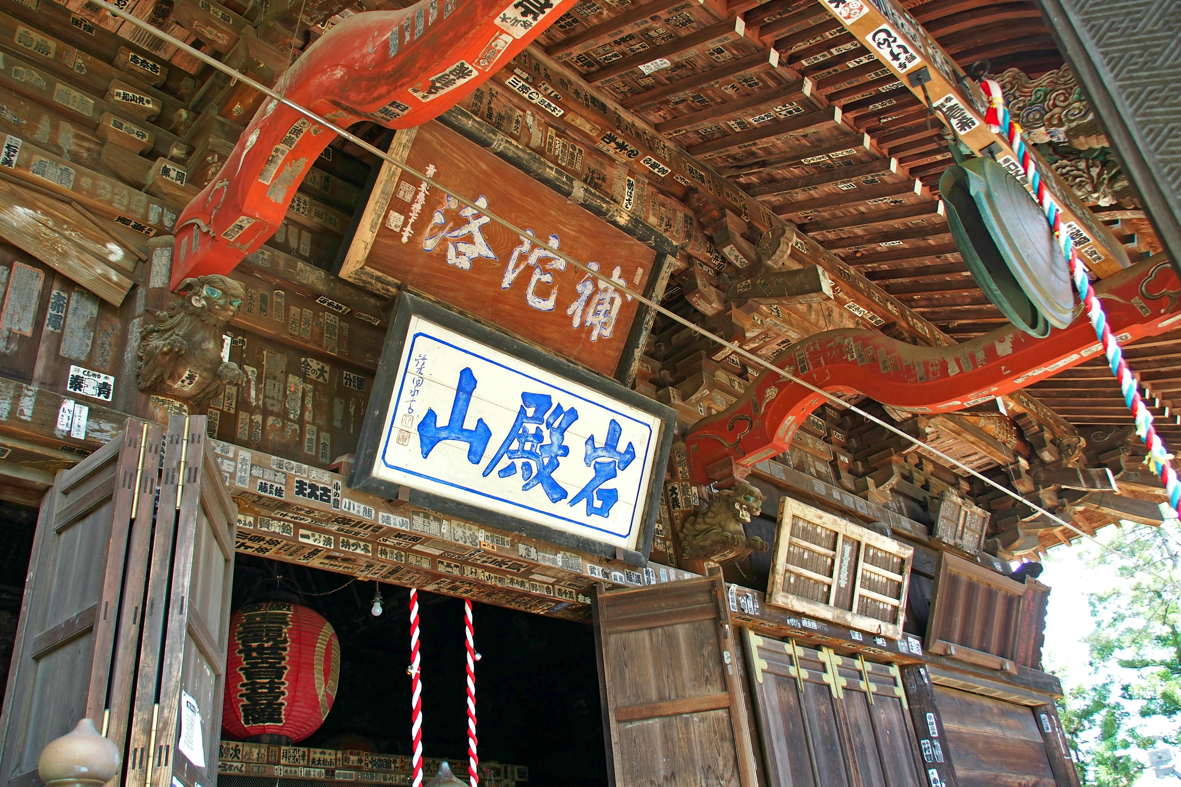 Entrance of an old shrine with wooden doors and decorative roof bright colored lanterns and ornaments visible