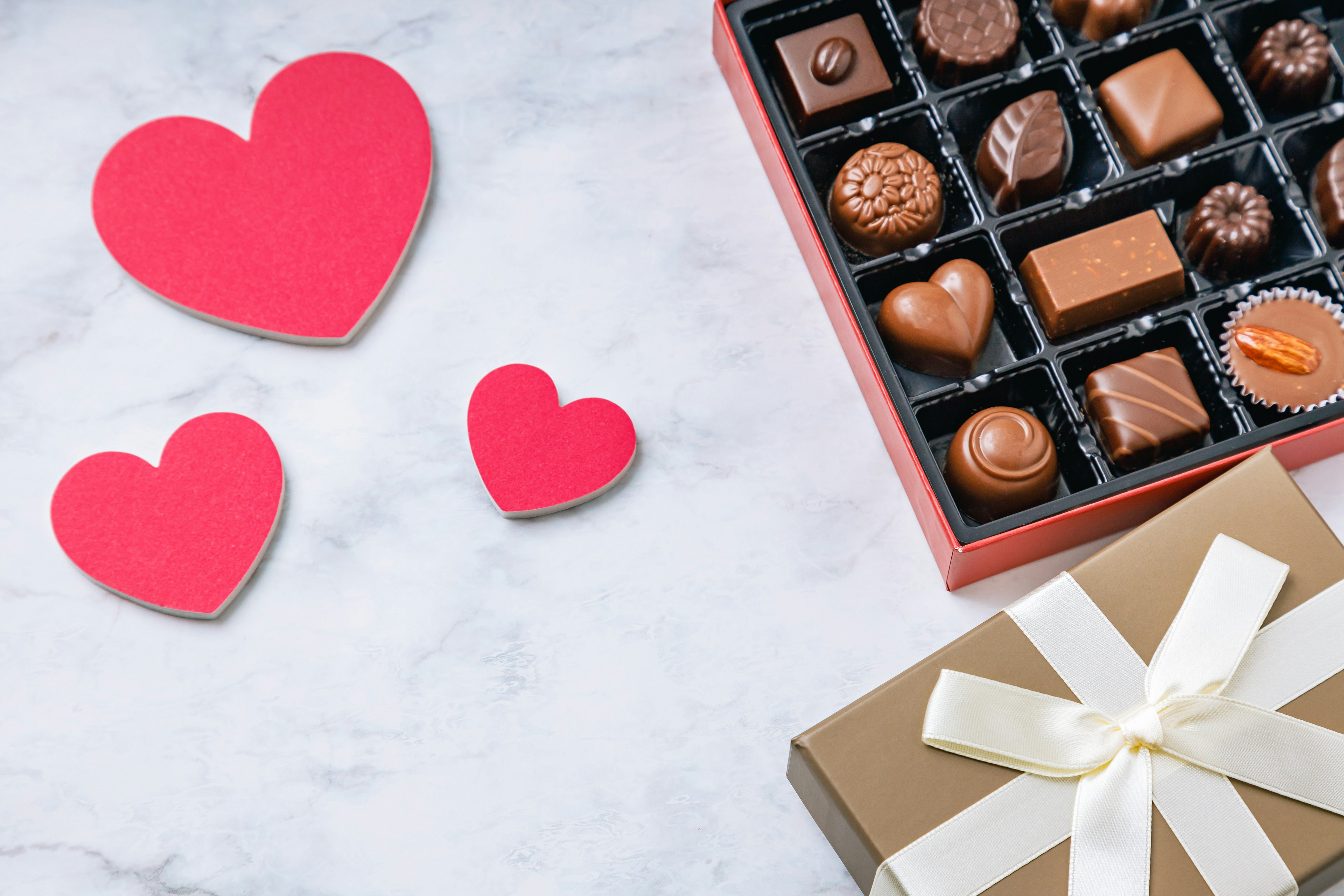 Tarjetas en forma de corazón rojo junto a una caja de chocolates surtidos