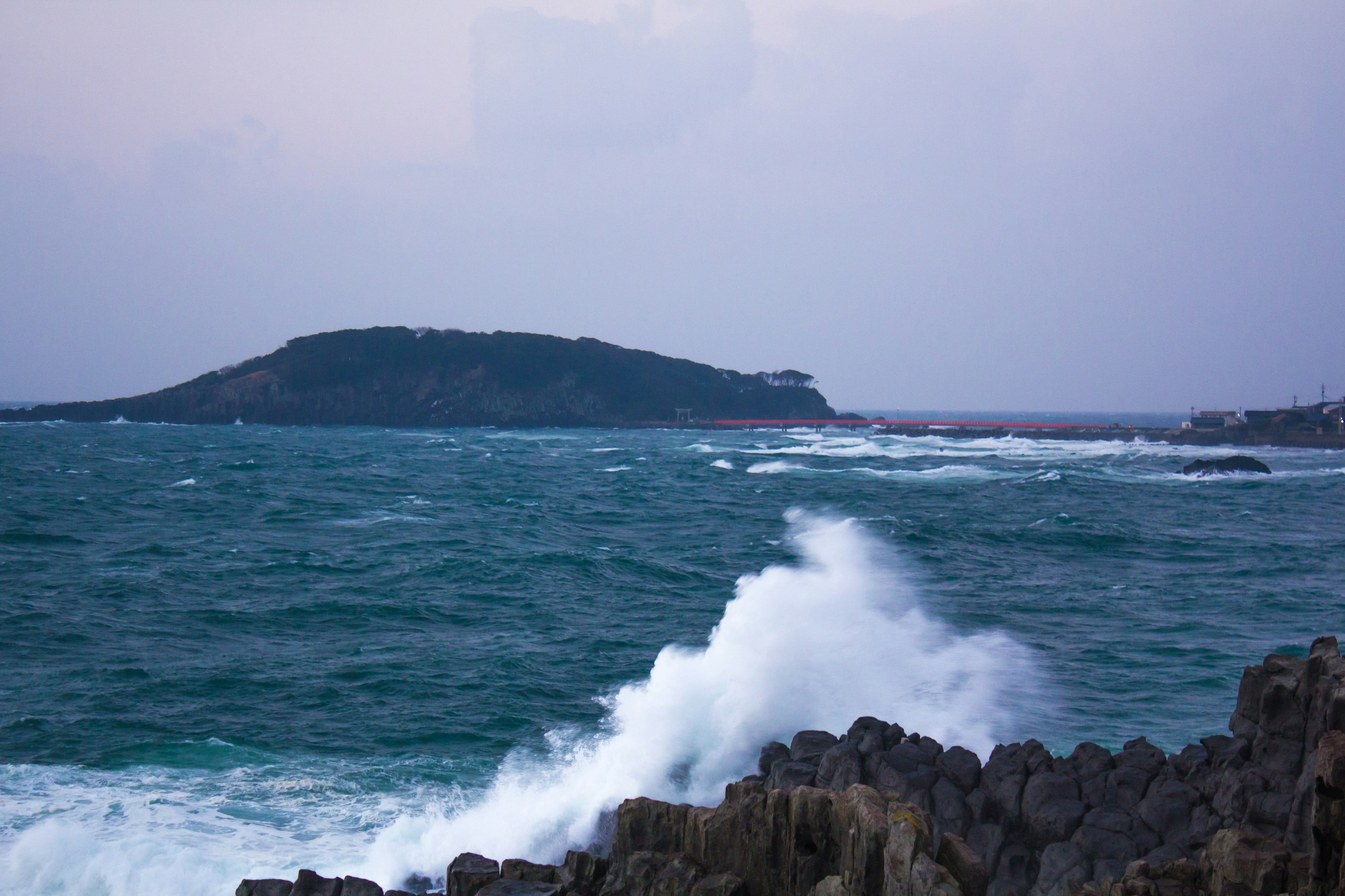 波浪拍打岩石，遠處有一個島