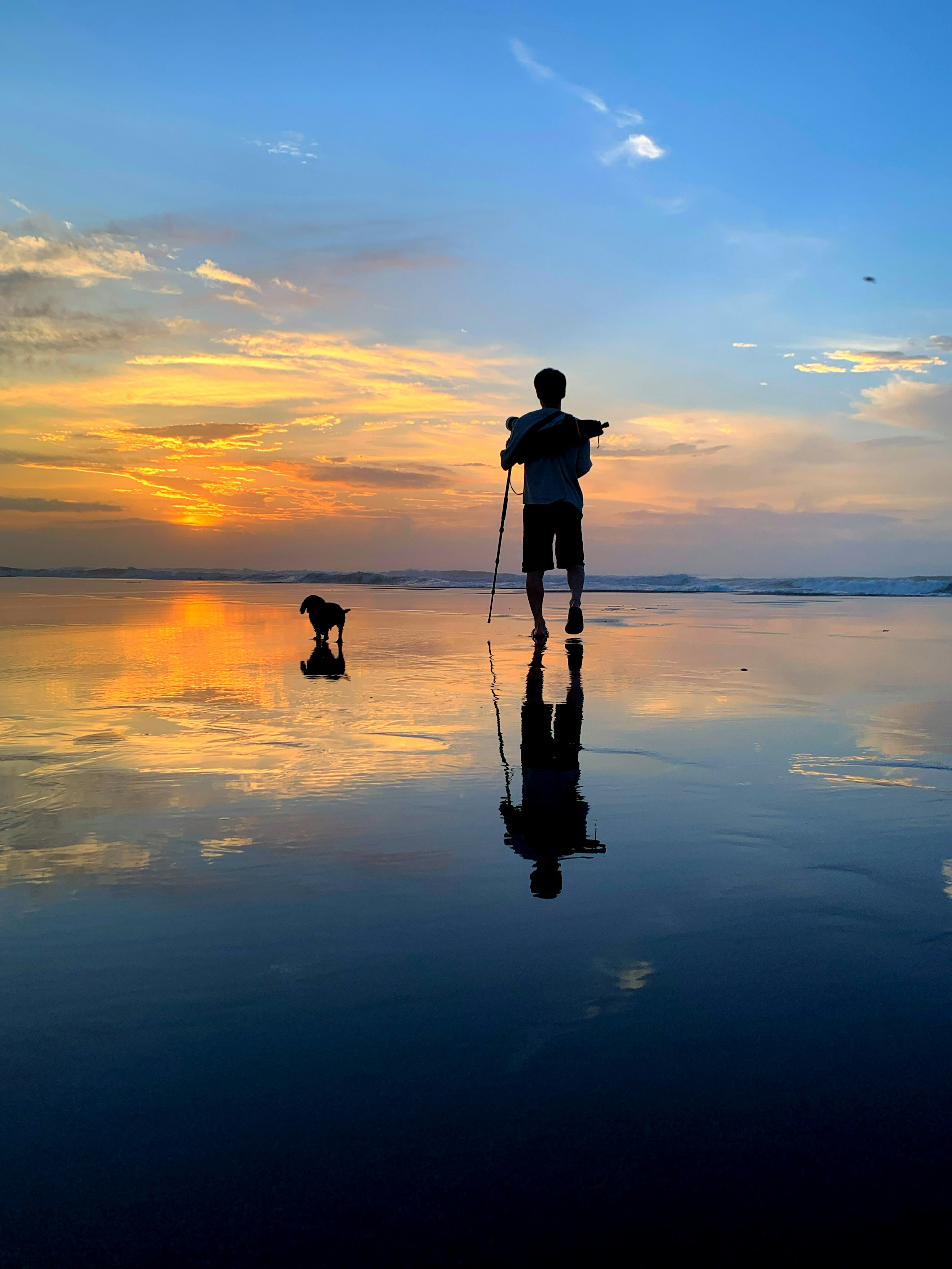 Silhouette eines Jungen und eines Hundes auf dem Wasser, das den Sonnenuntergang reflektiert