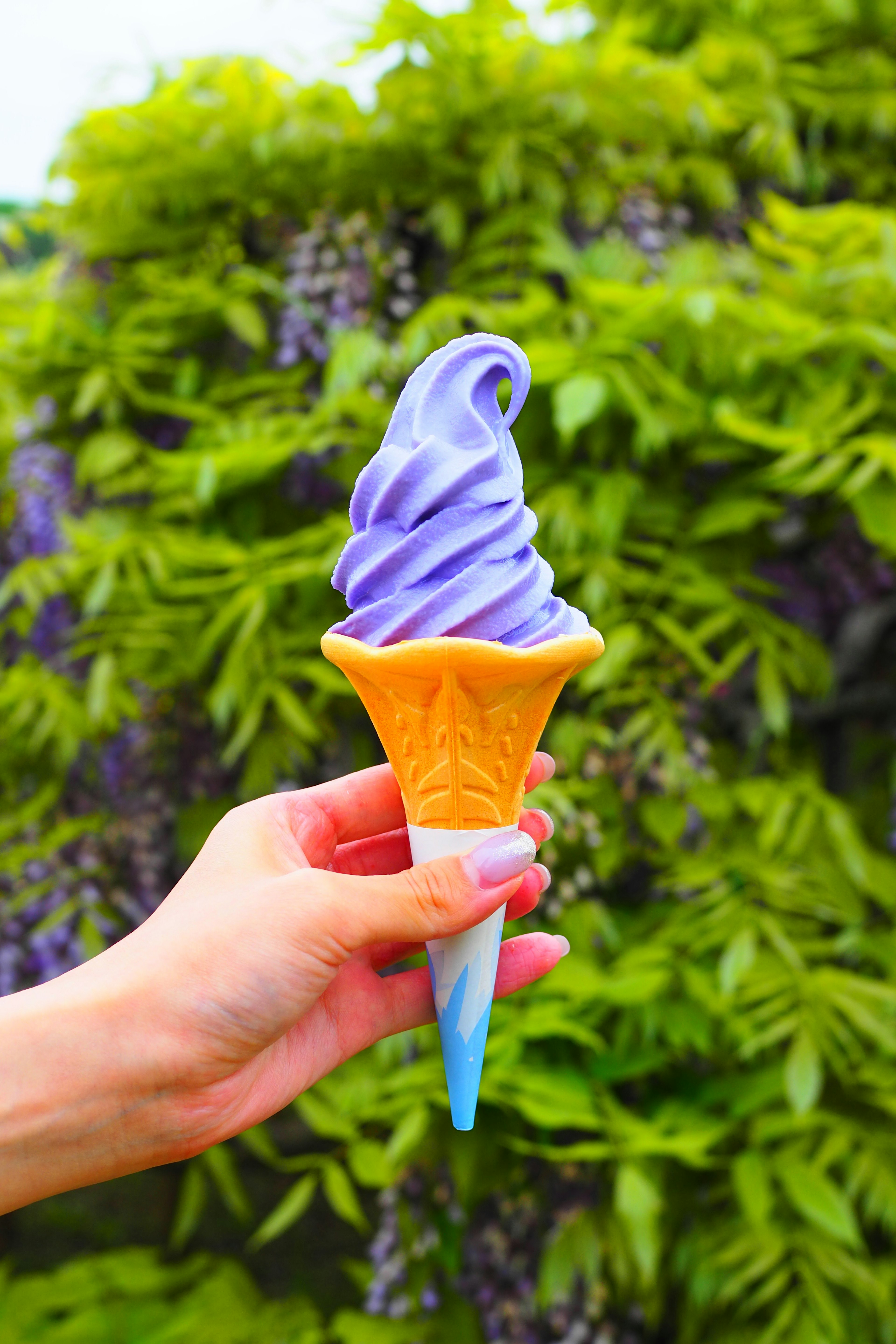 Hand holding a purple soft serve ice cream cone with a green backdrop