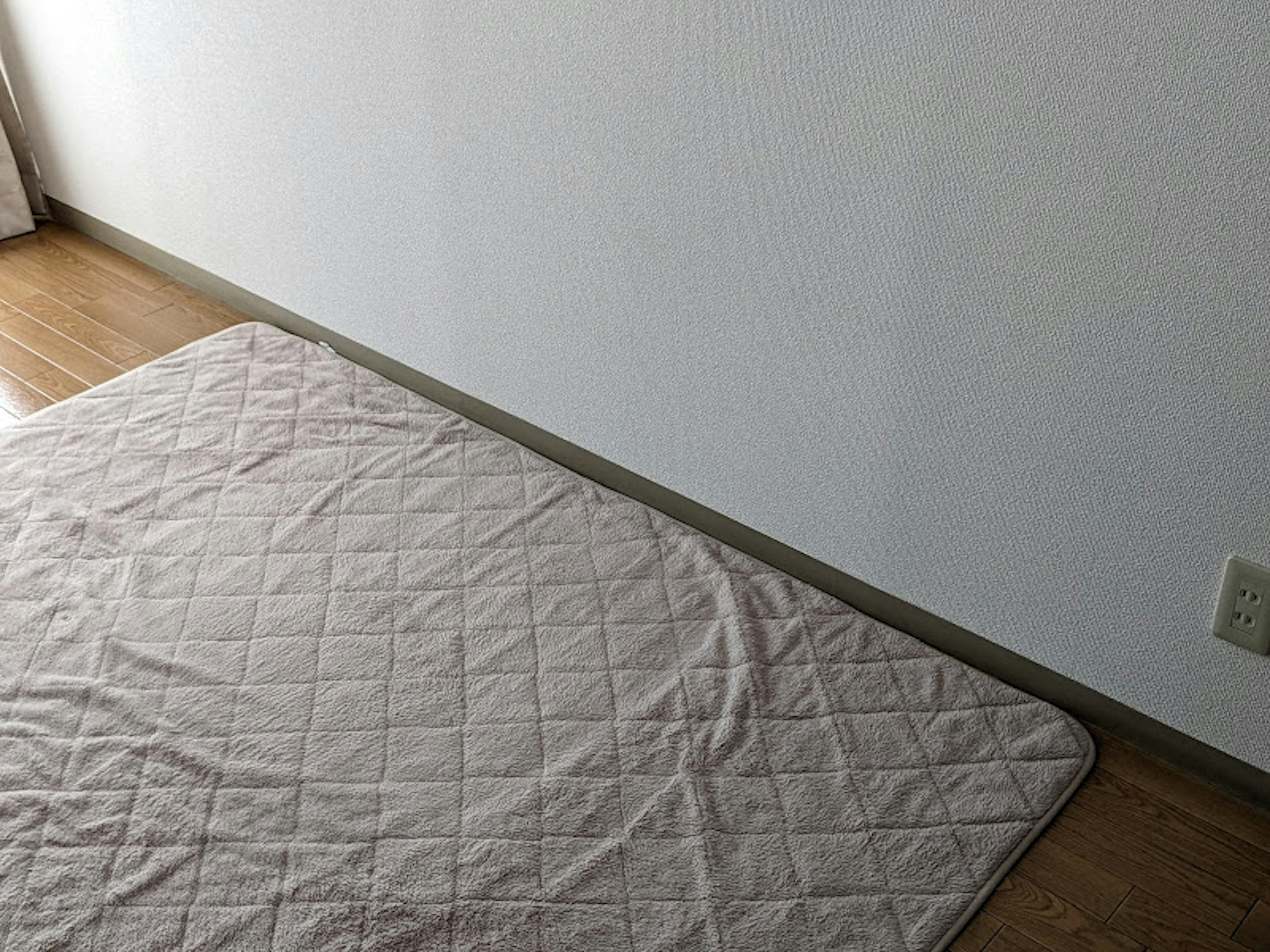 Cream-colored bedding on a wooden floor in a room corner