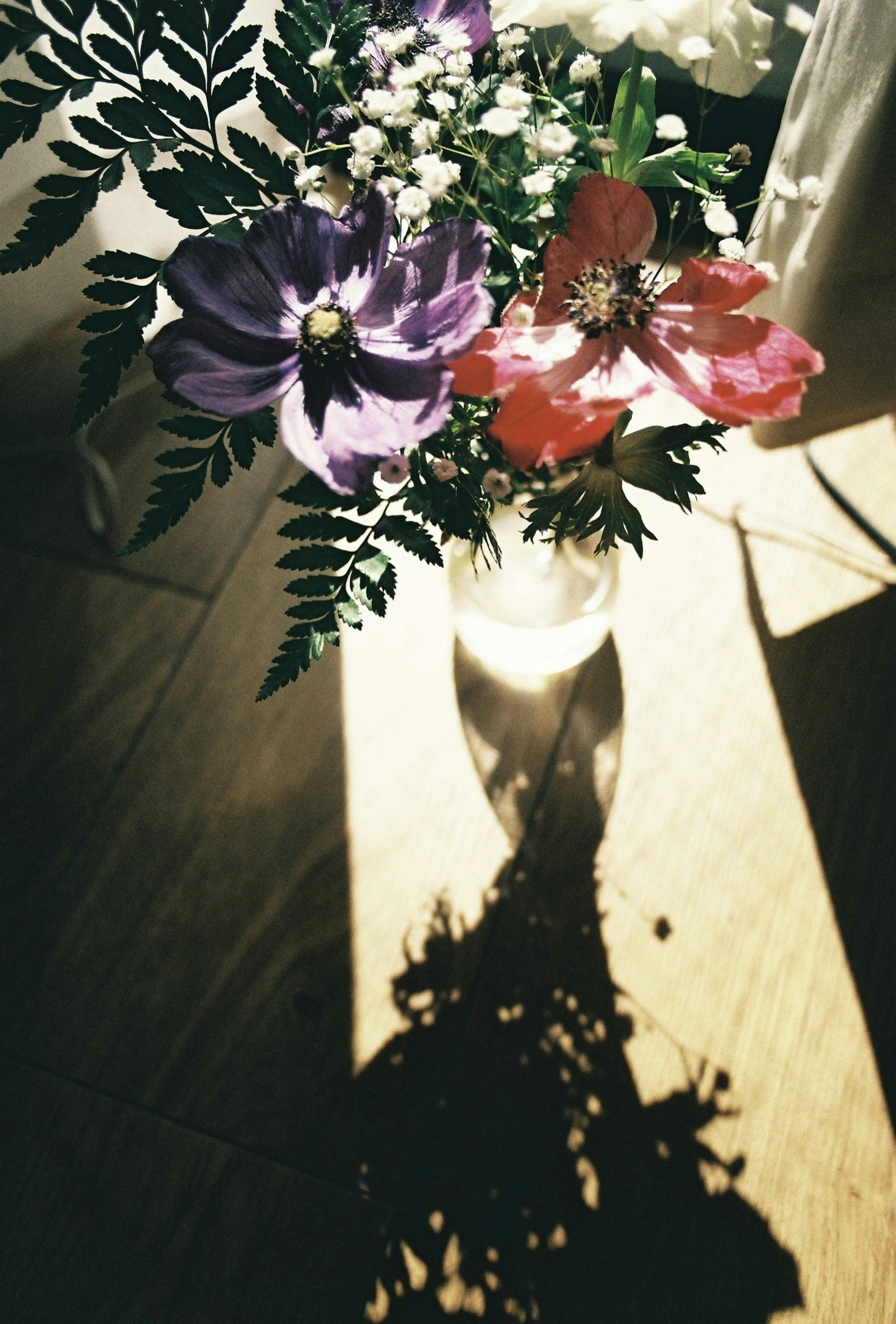 Ein bunter Blumenstrauß in einer Vase, der einen Schatten auf eine Holzoberfläche wirft