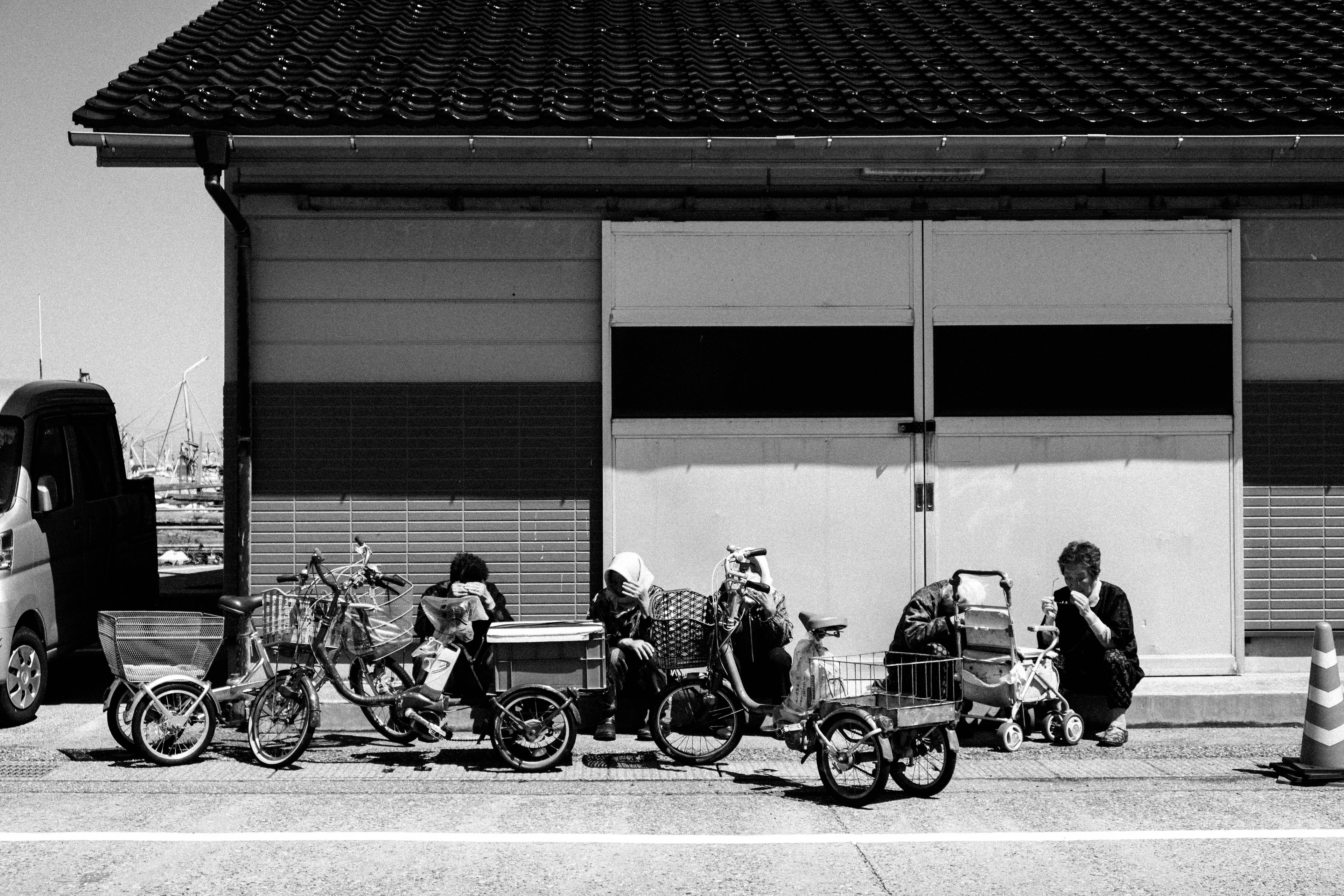 Black and white image showing several bicycles lined up with children playing nearby