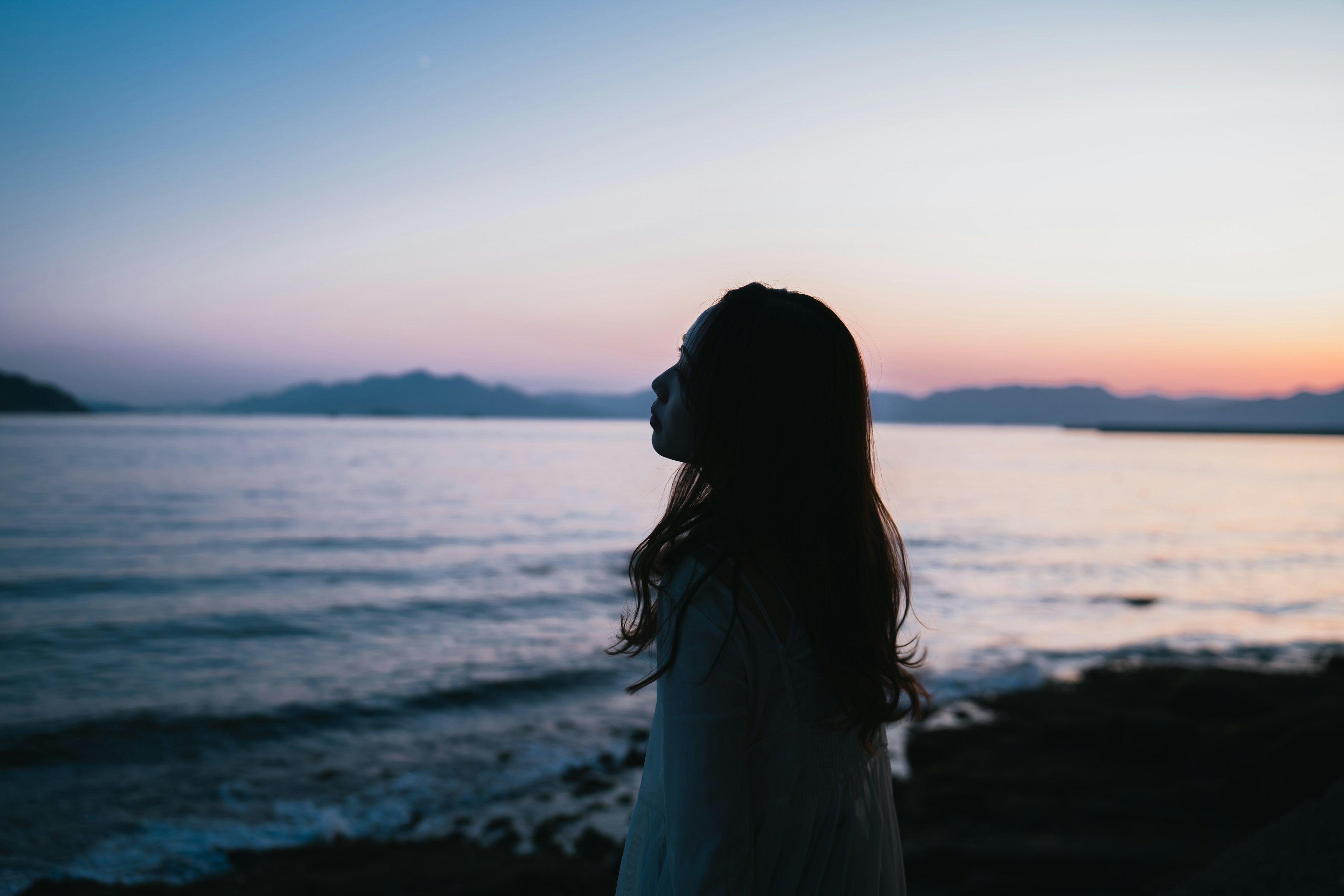 夕暮れの海辺で佇む女性のシルエット