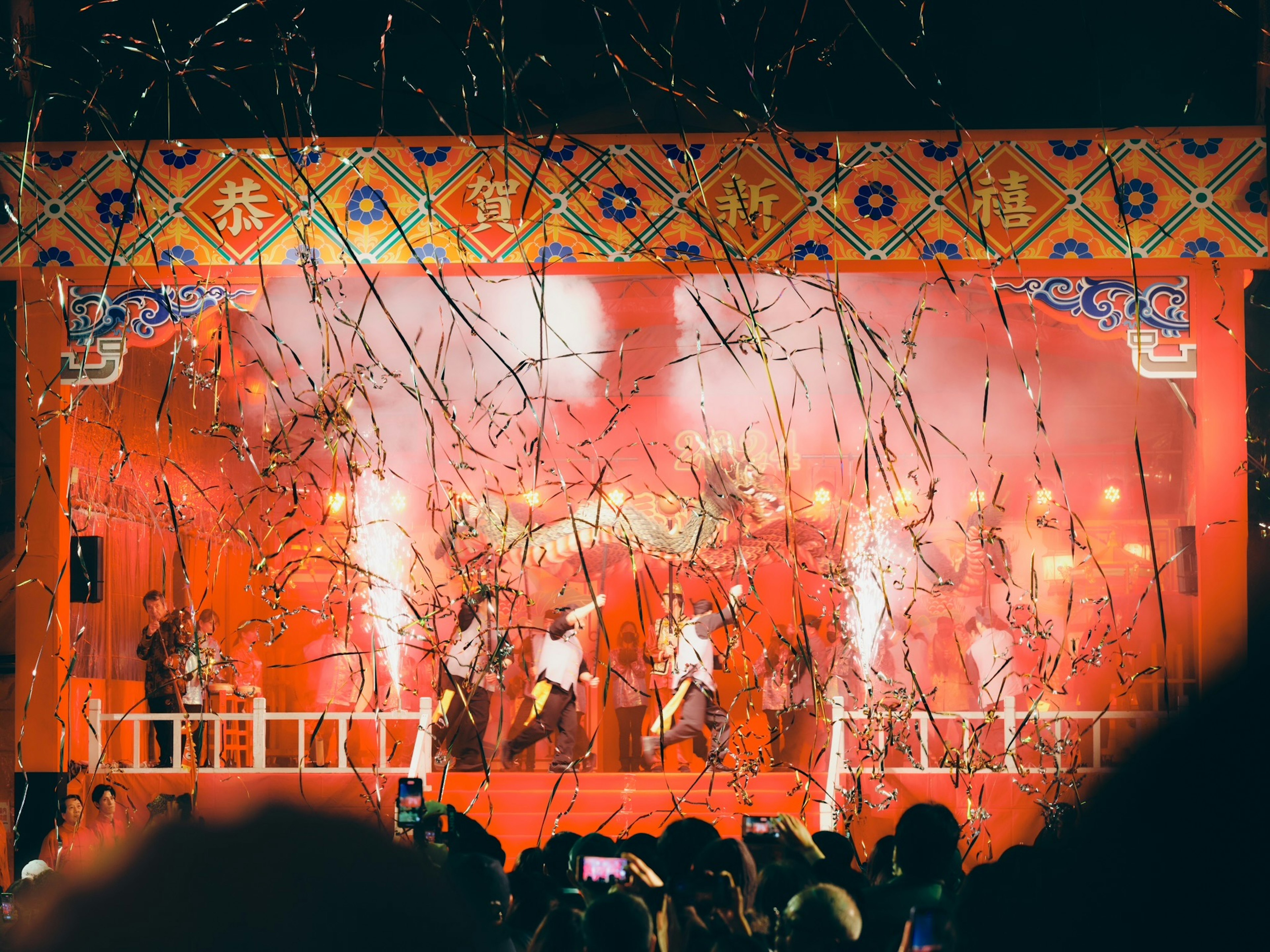 Performers on stage with a vibrant red backdrop and fireworks display