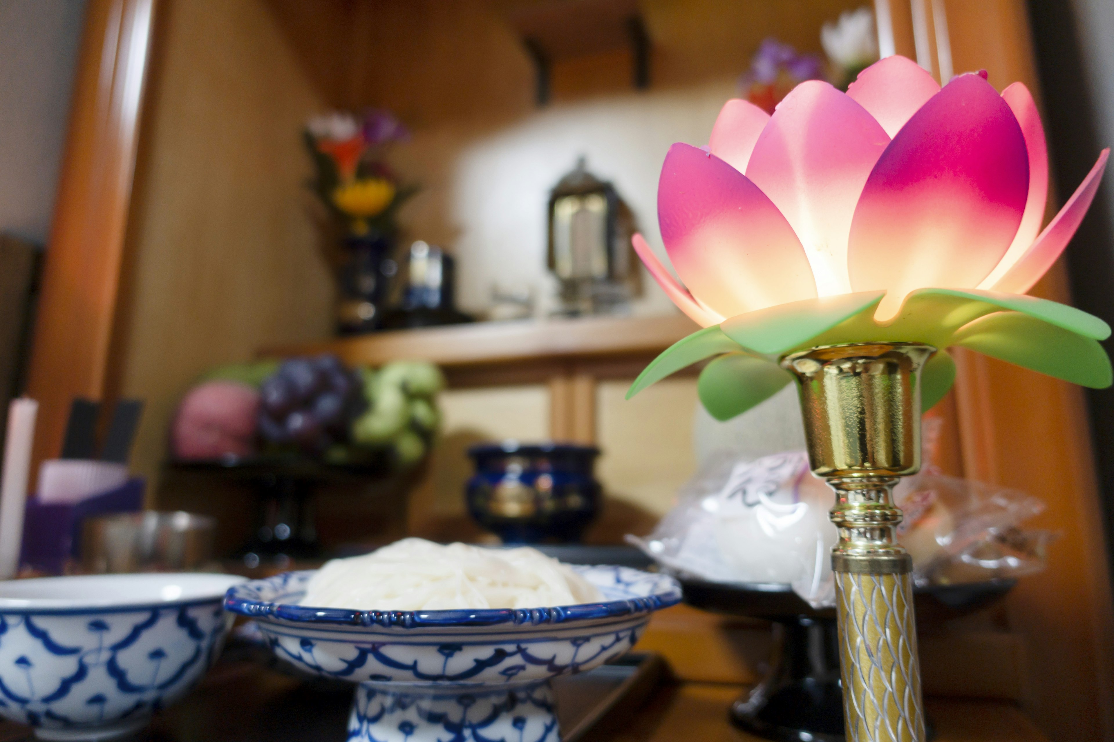 Lotuslampe mit rosa Blütenblättern auf einem Altar umgeben von Reisschalen und bunten Blumen