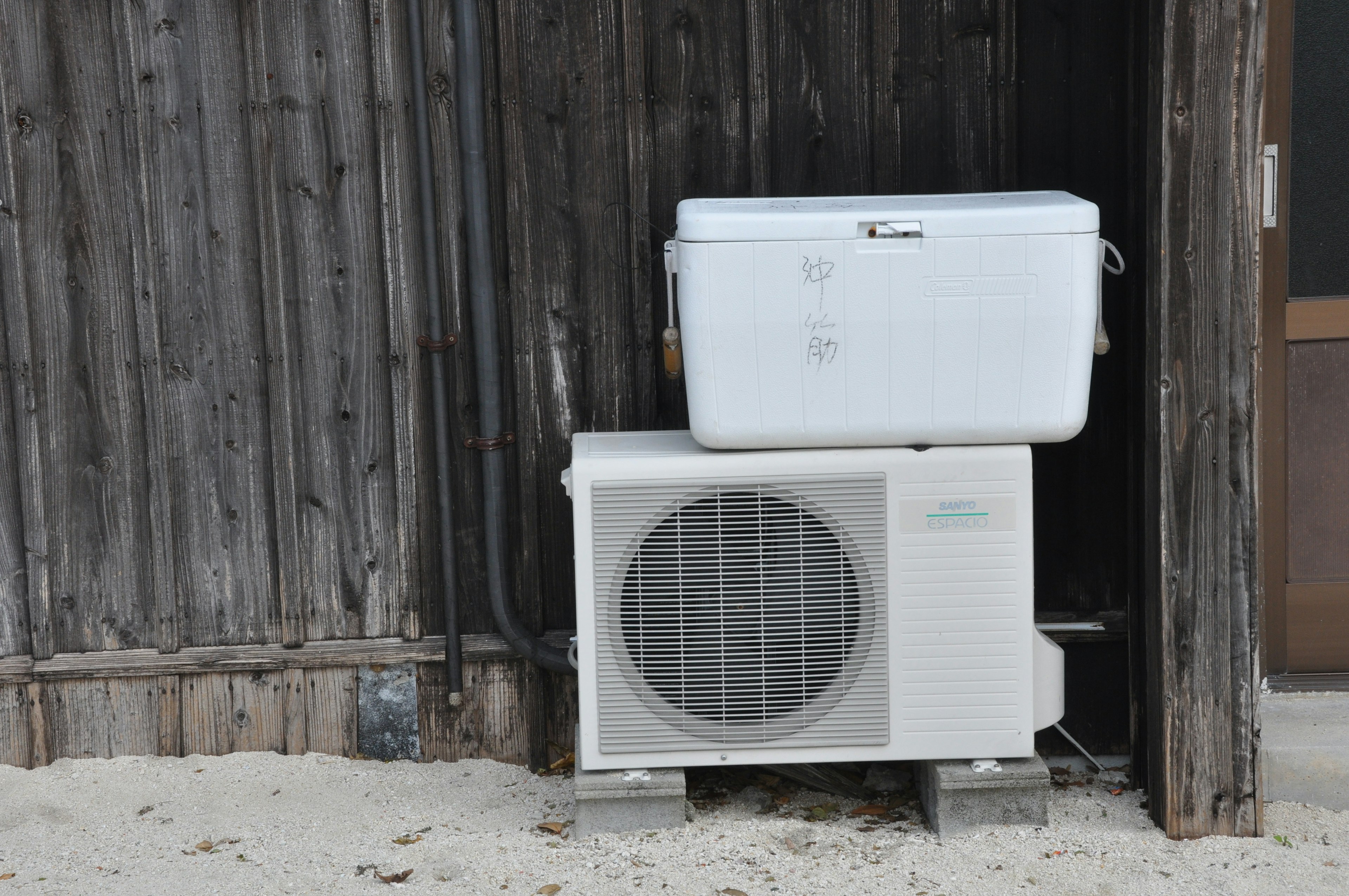 Air conditioning unit mounted on a wooden wall with a white cooler on top