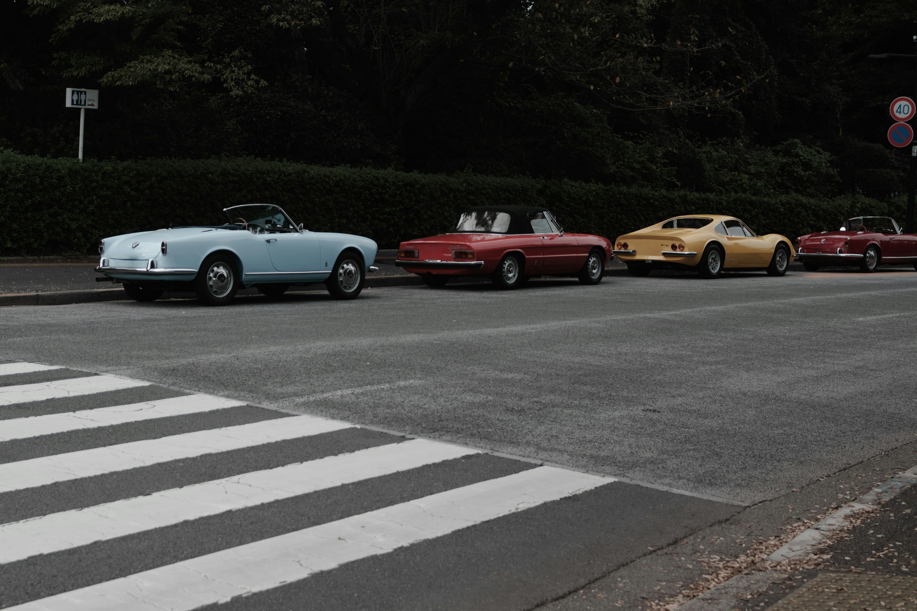 Una fila de coches clásicos incluyendo un convertible azul y coches deportivos rojos en una calle