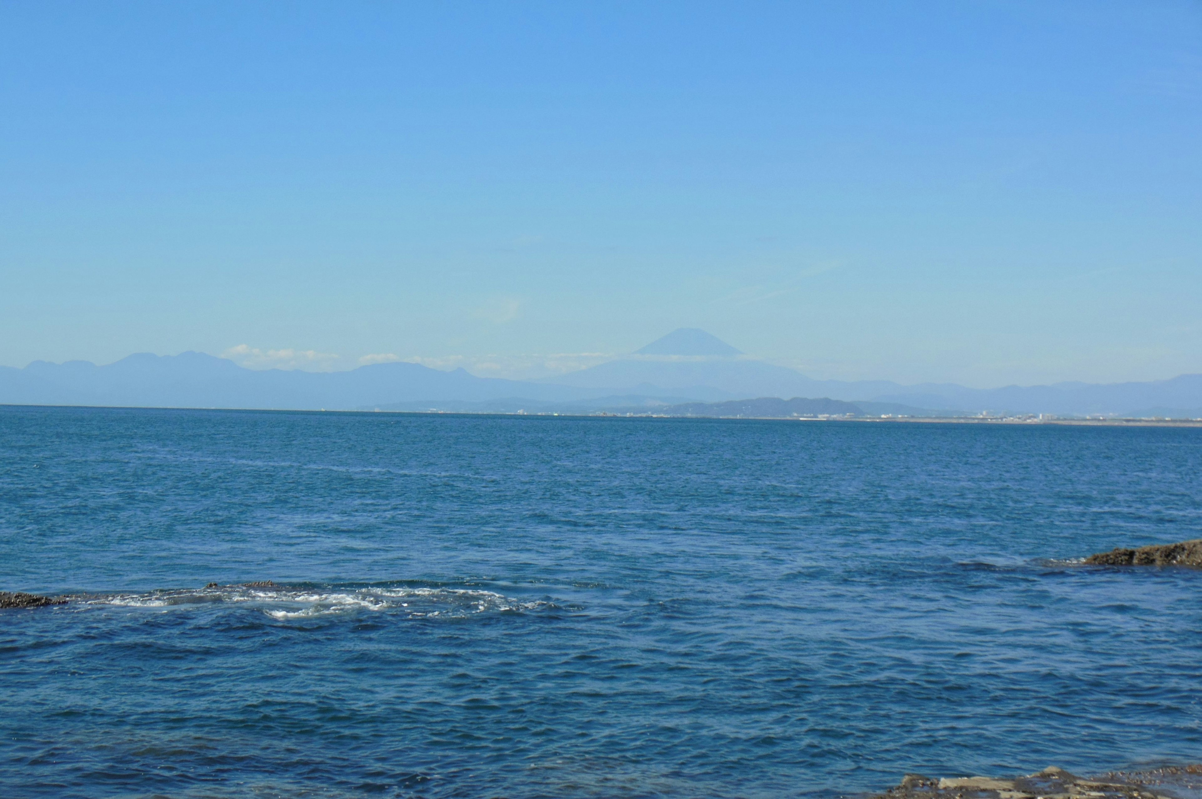 Pemandangan laut dan langit biru dengan gunung di kejauhan