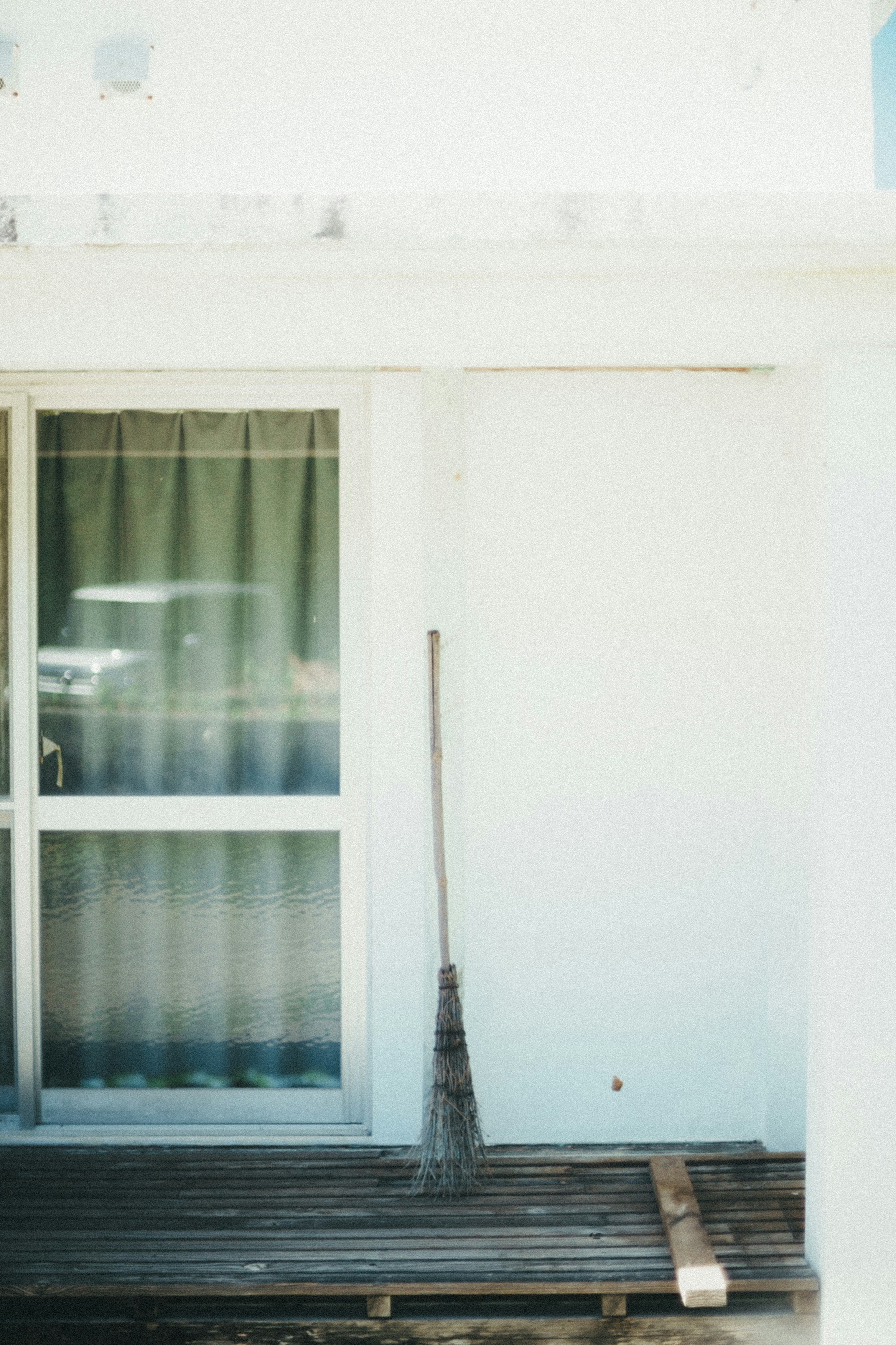 Broom standing against a white wall with a window and curtains